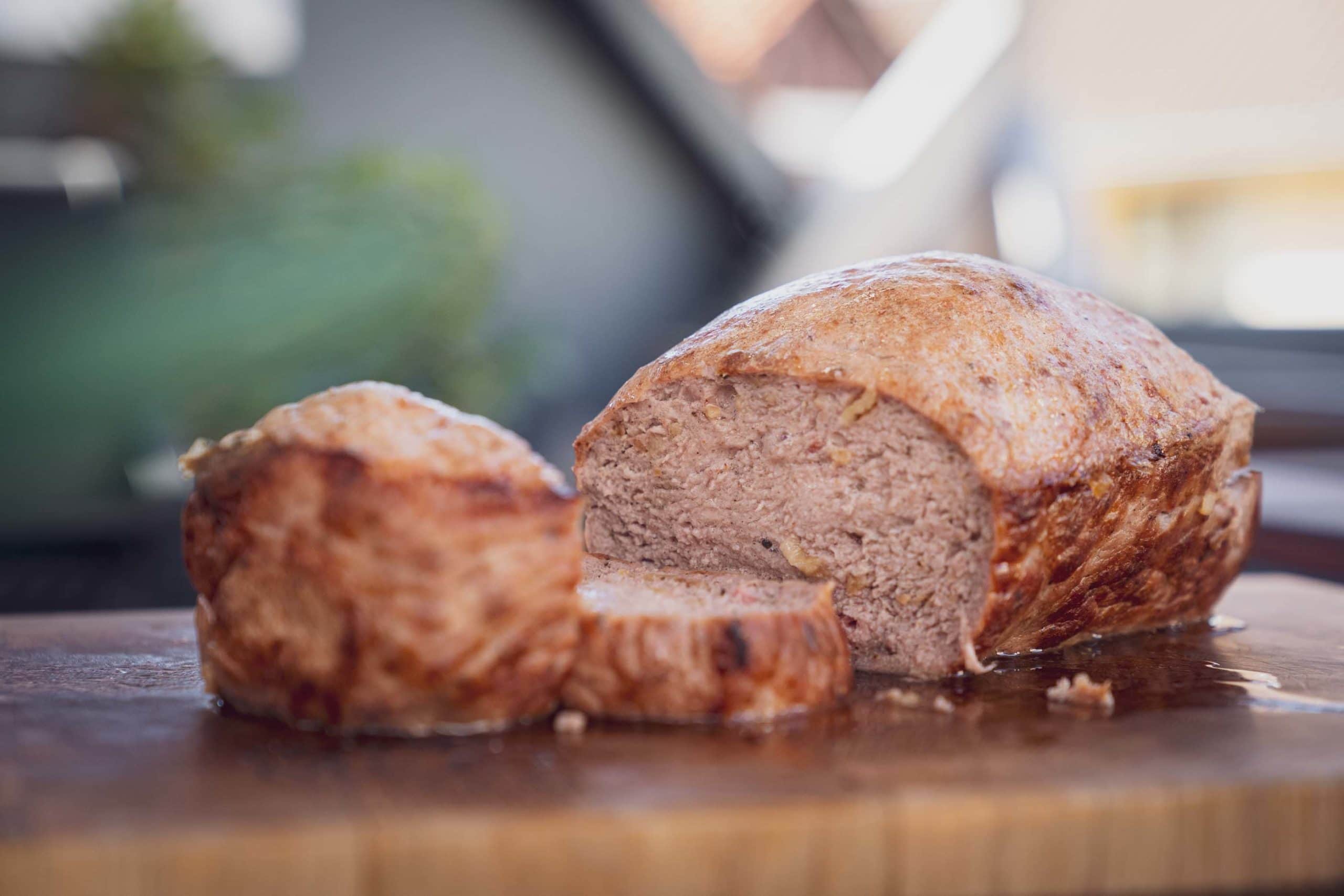 Saftiger, selbstgemachter Leberkäse aufgeschnitten mit feiner Kruste auf einem Holzbrett