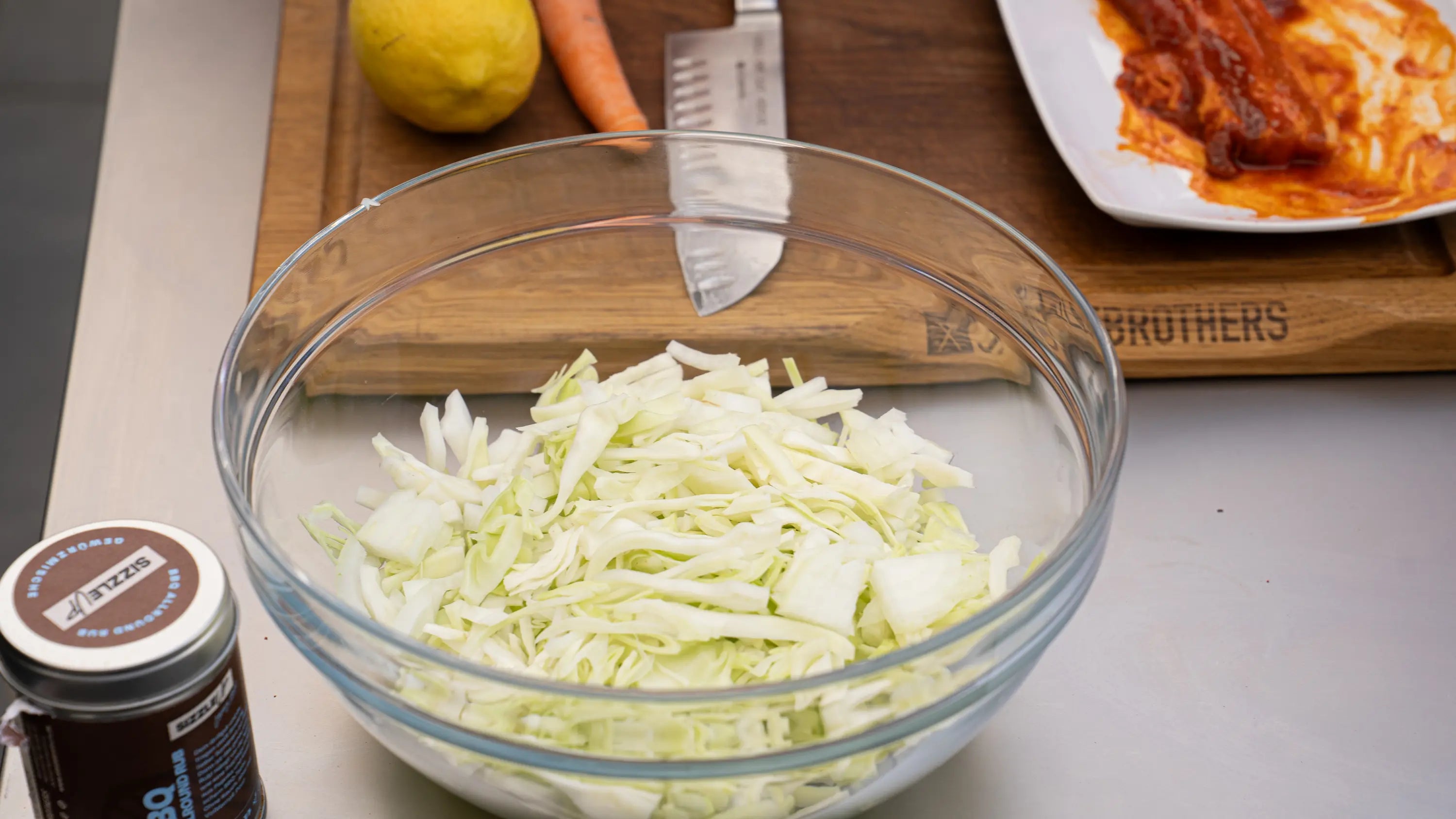 Glasschüssel mit geschnittenem Kohl, Karotte und Zitrone auf einem Brett mit Messer.