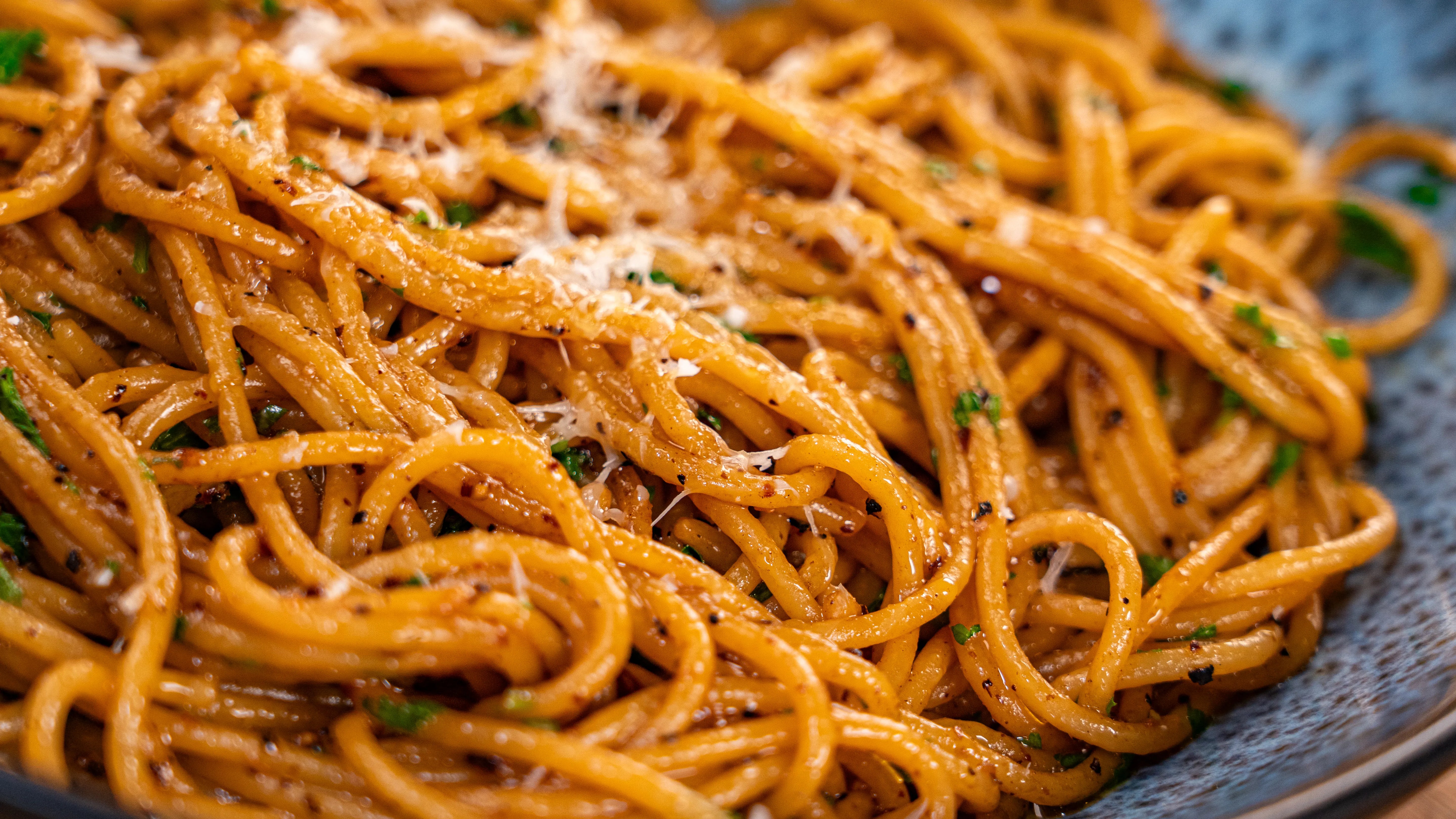 Spaghetti mit Kräutern und geriebenem Käse in Nahaufnahme.