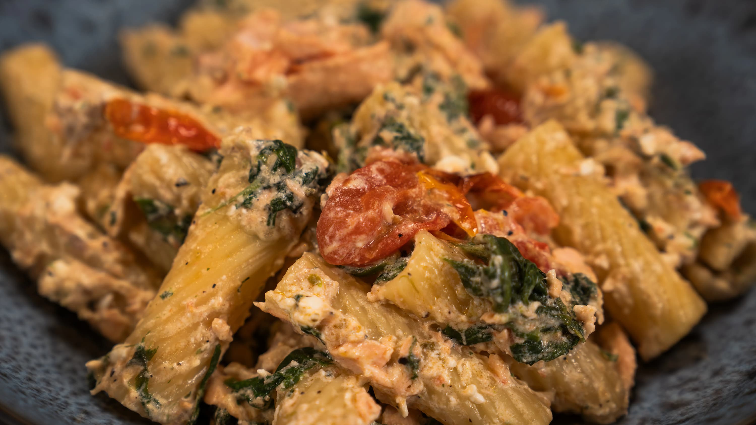 Nahaufnahme von Pasta mit Lachs, Spinat, Tomaten in cremiger Sauce.