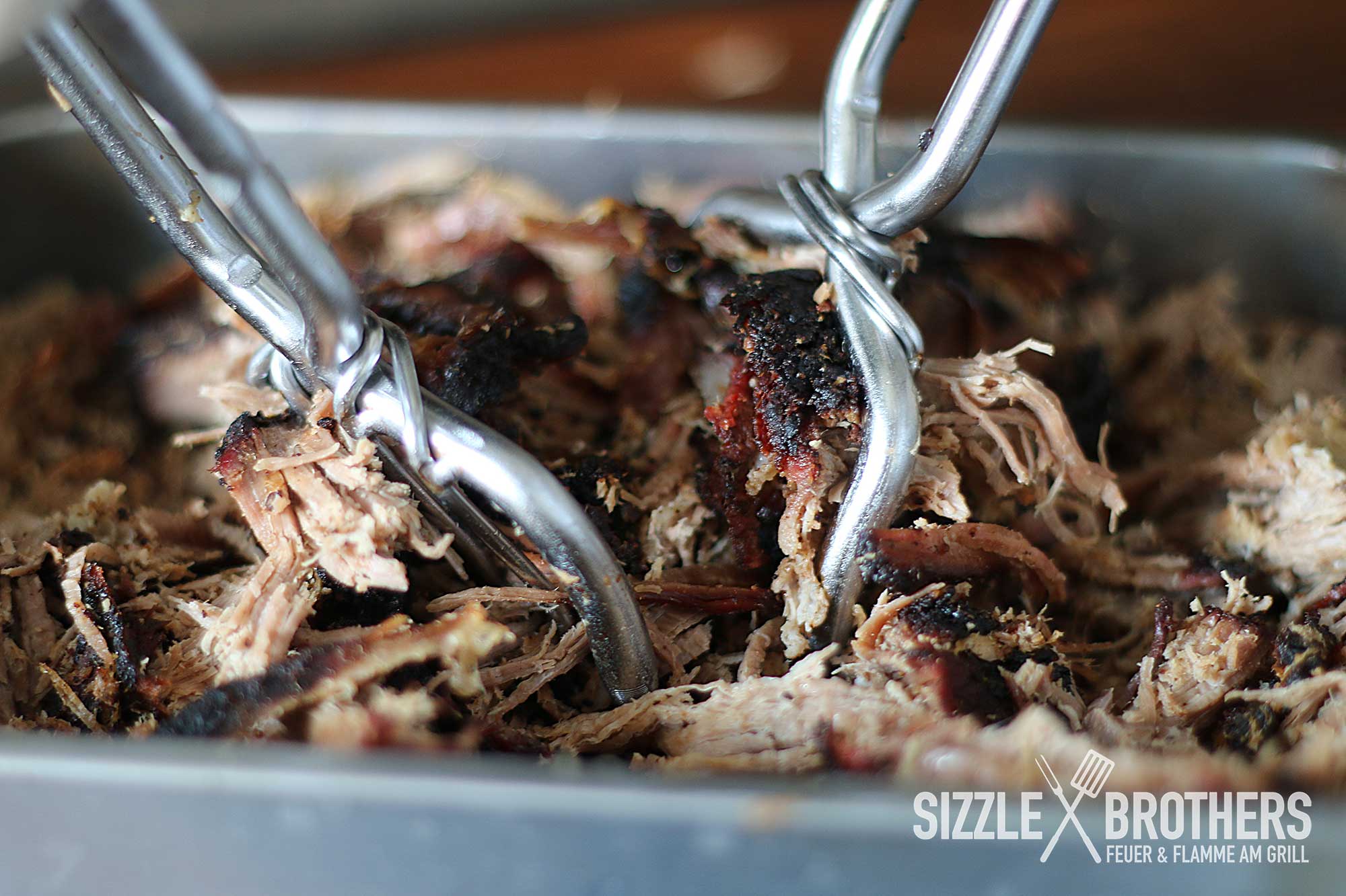Zwei Metallgabeln zerkleinern saftiges Pulled Pork in einer Schale.