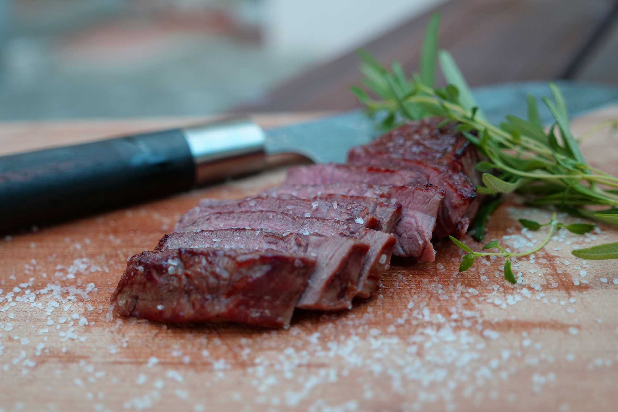 Dünn geschnittenes Steak mit Kräutern und Salz auf einem Holzbrett.