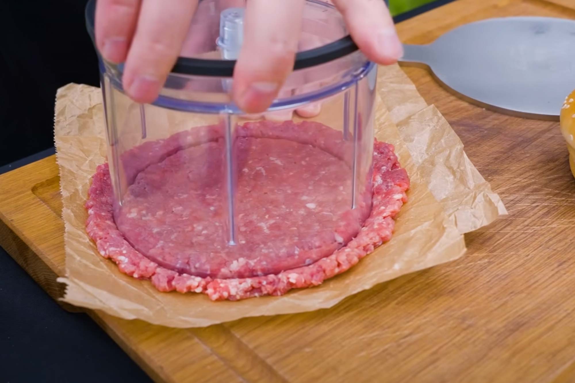 Presse formt rohes Hackfleisch auf braunem Papier auf einem Holzbrett.