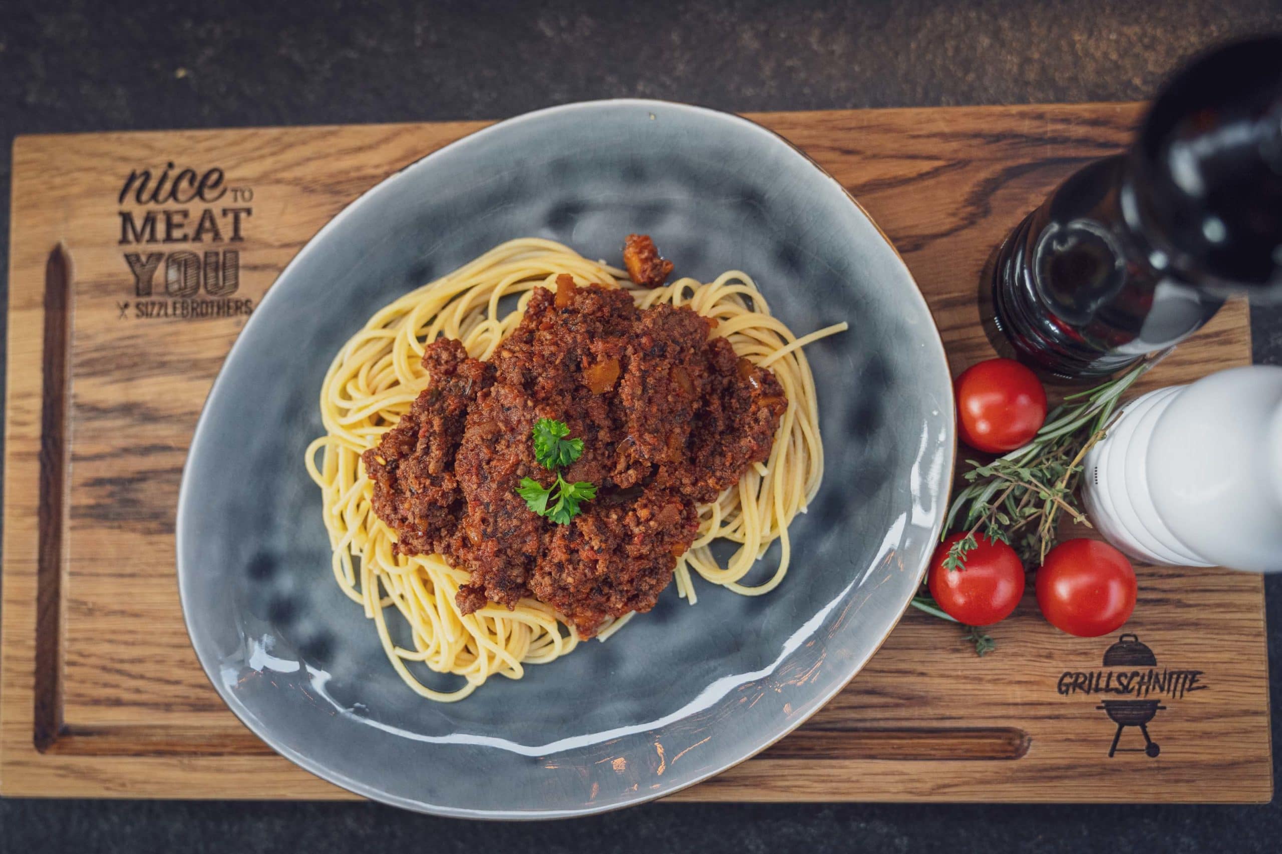 Spaghetti mit Hackfleischsoße auf Teller, umgeben von Tomaten und Gewürzen.