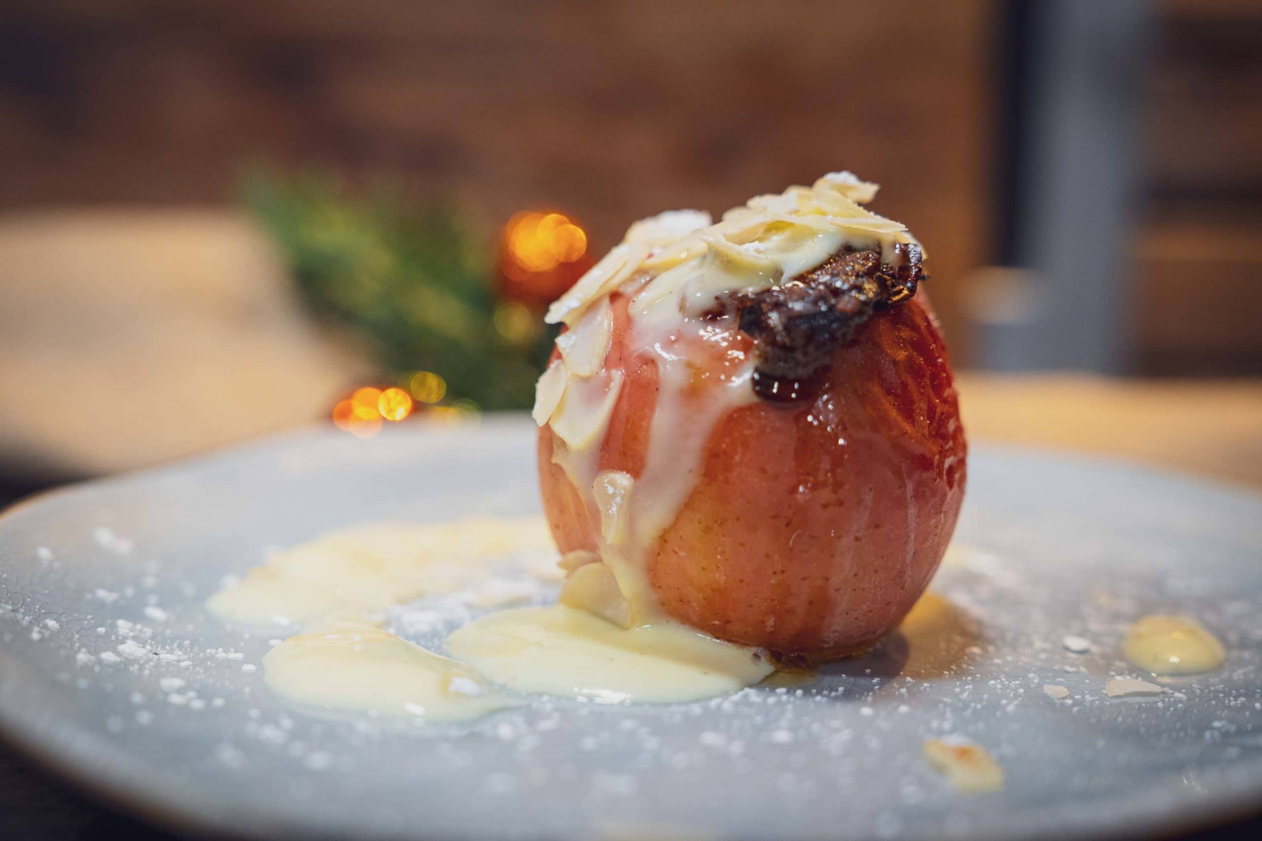 Ein gebratener Apfel mit weißer Soße und Mandelsplittern auf einem Teller.