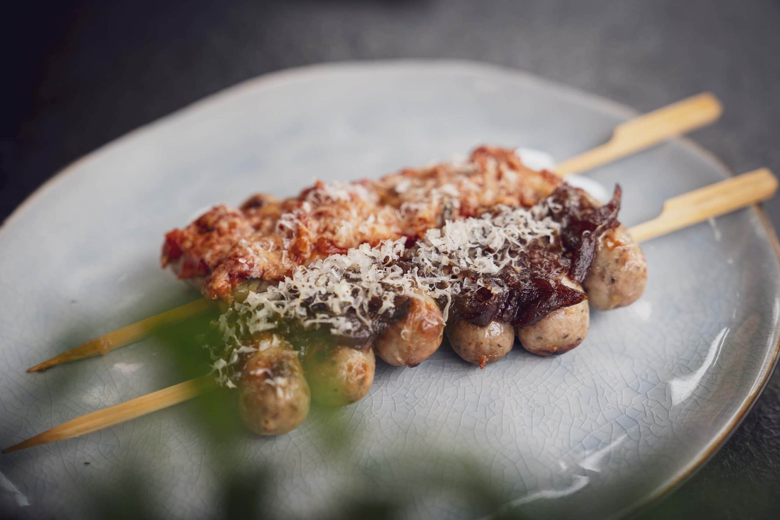 Zwei Spieße mit gegrilltem Fleisch und geriebenem Käse auf grauem Teller.
