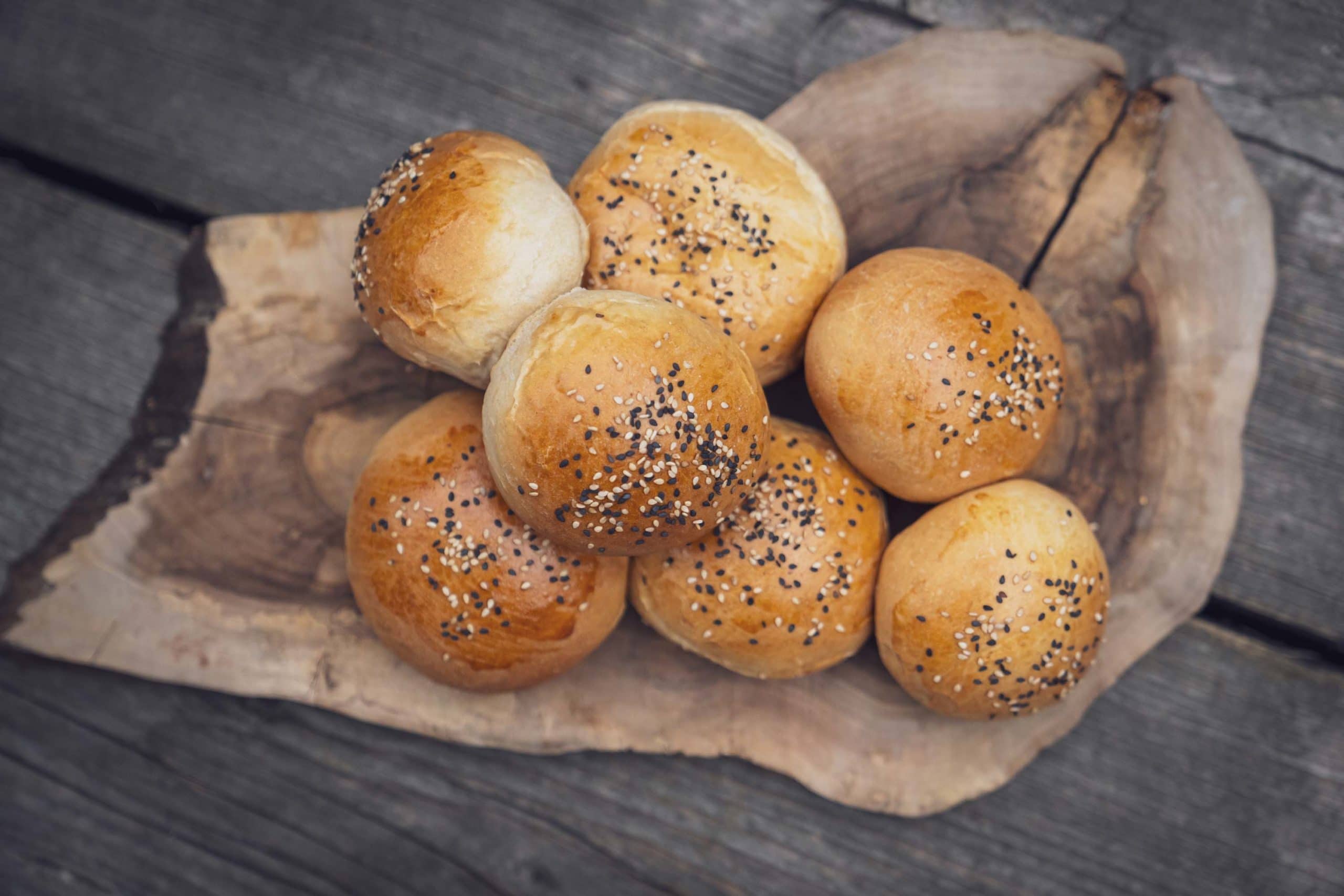 Mehrere runde Brötchen mit Sesam auf einem Holzbrett.