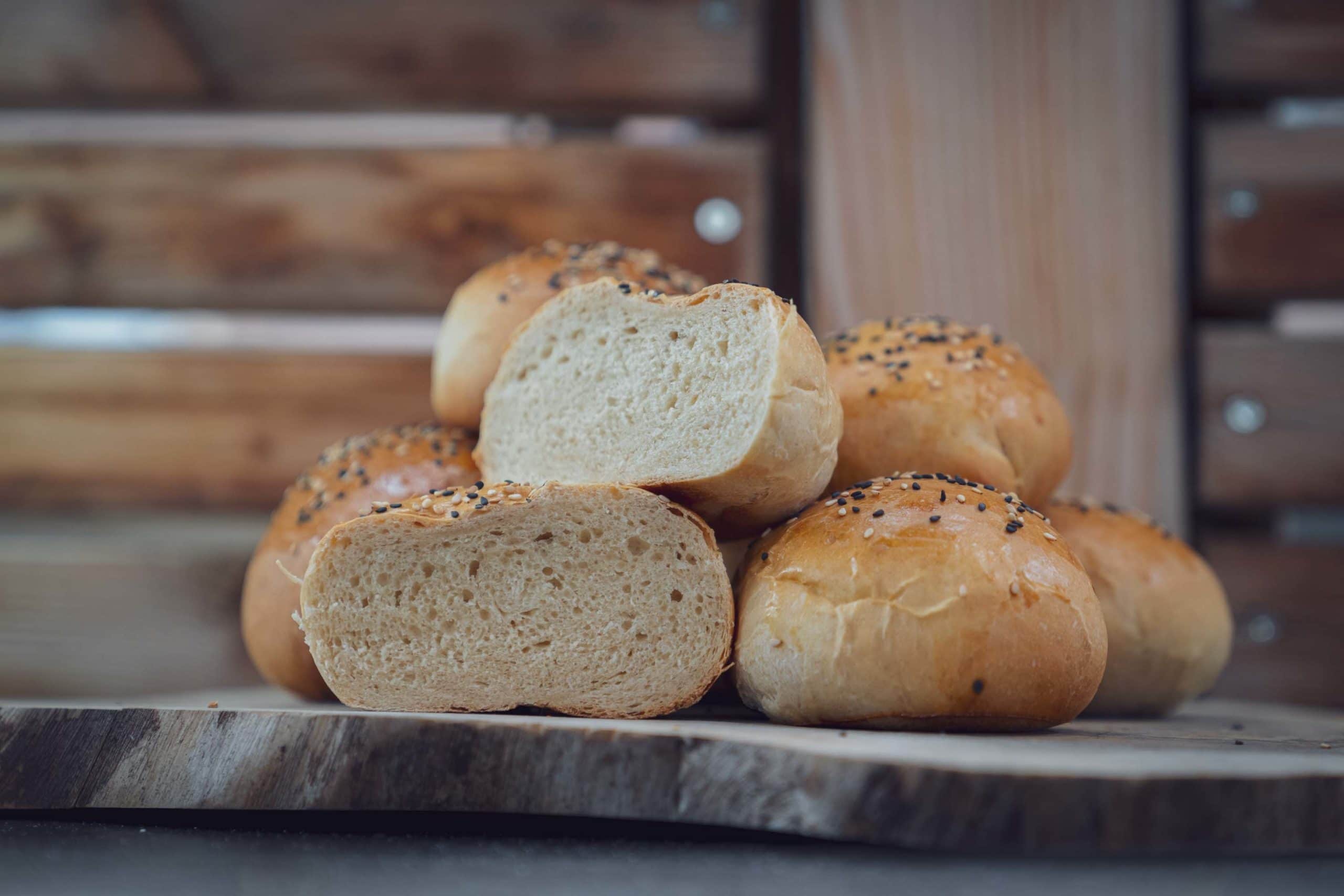 Ein Stapel goldbrauner Brötchen mit Sesam auf Holzbrett.