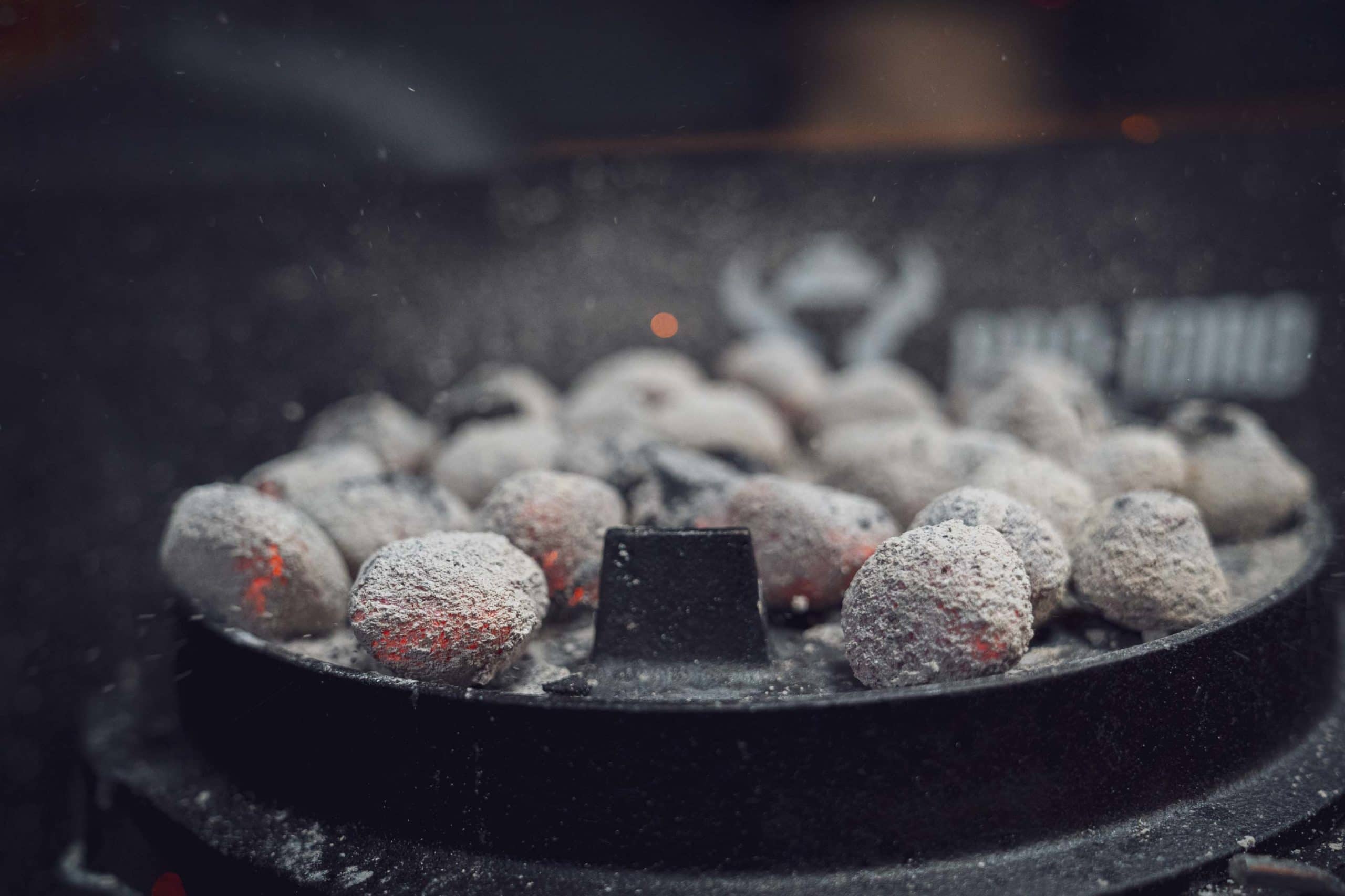 Naheaufnahme von glühenden Kohlebriketts auf einem Grill, teilweise mit Asche bedeckt.