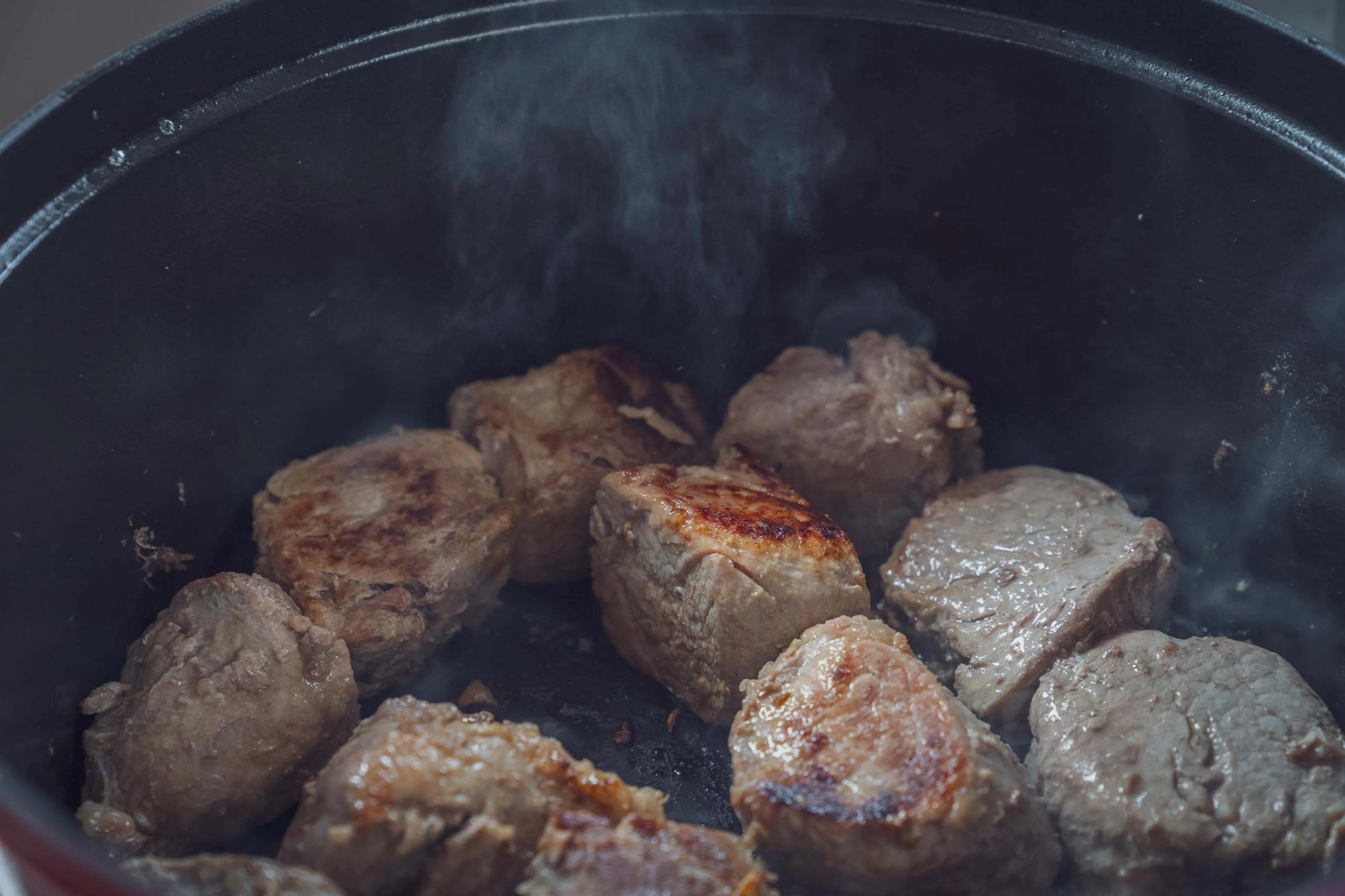 Fleischstücke braten in einem Topf, Rauch steigt auf.
