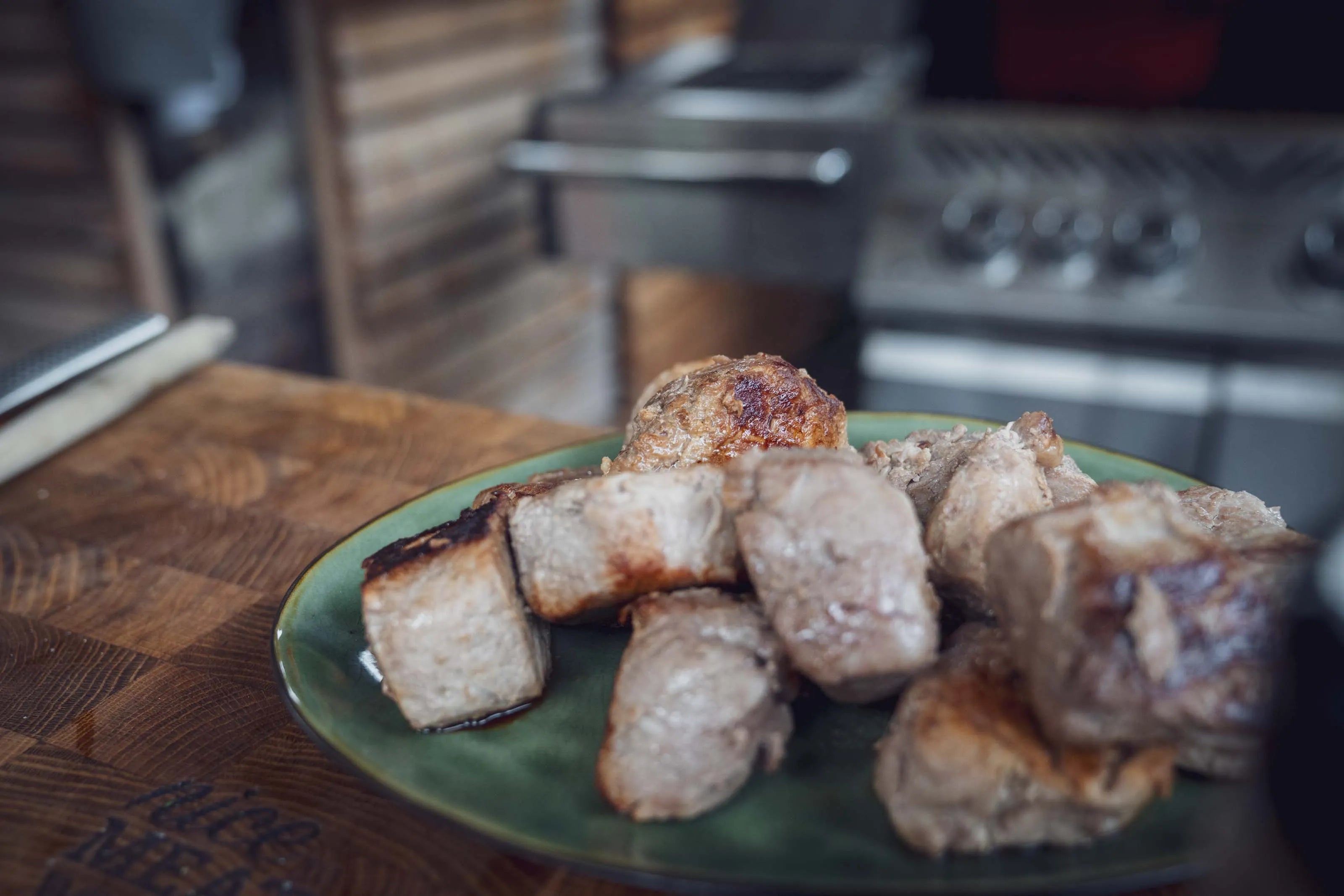 Gekochte Fleischstücke auf einem grünen Teller auf einem Küchenbrett.