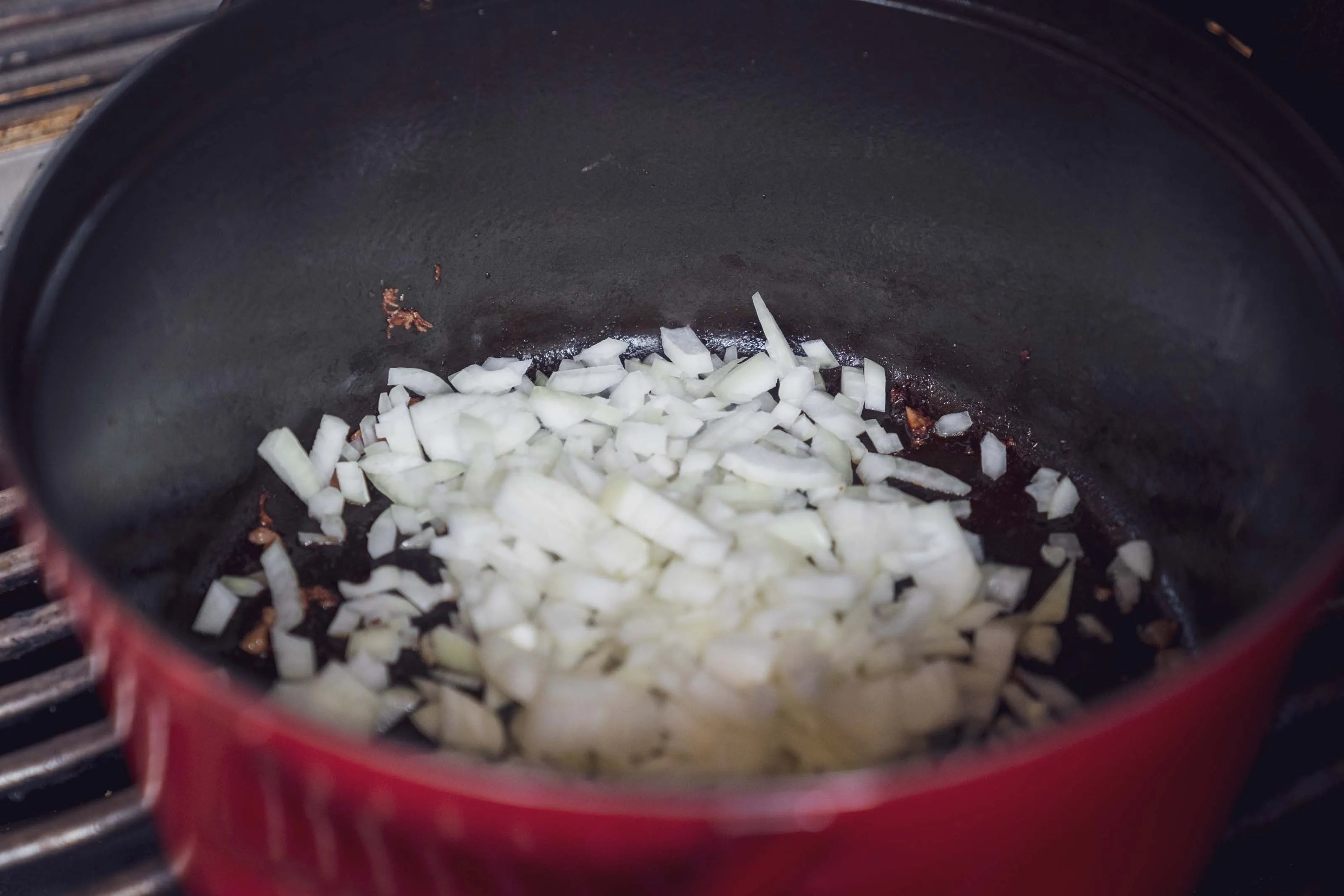 Gehackte Zwiebeln in einem roten Topf auf dem Herd.