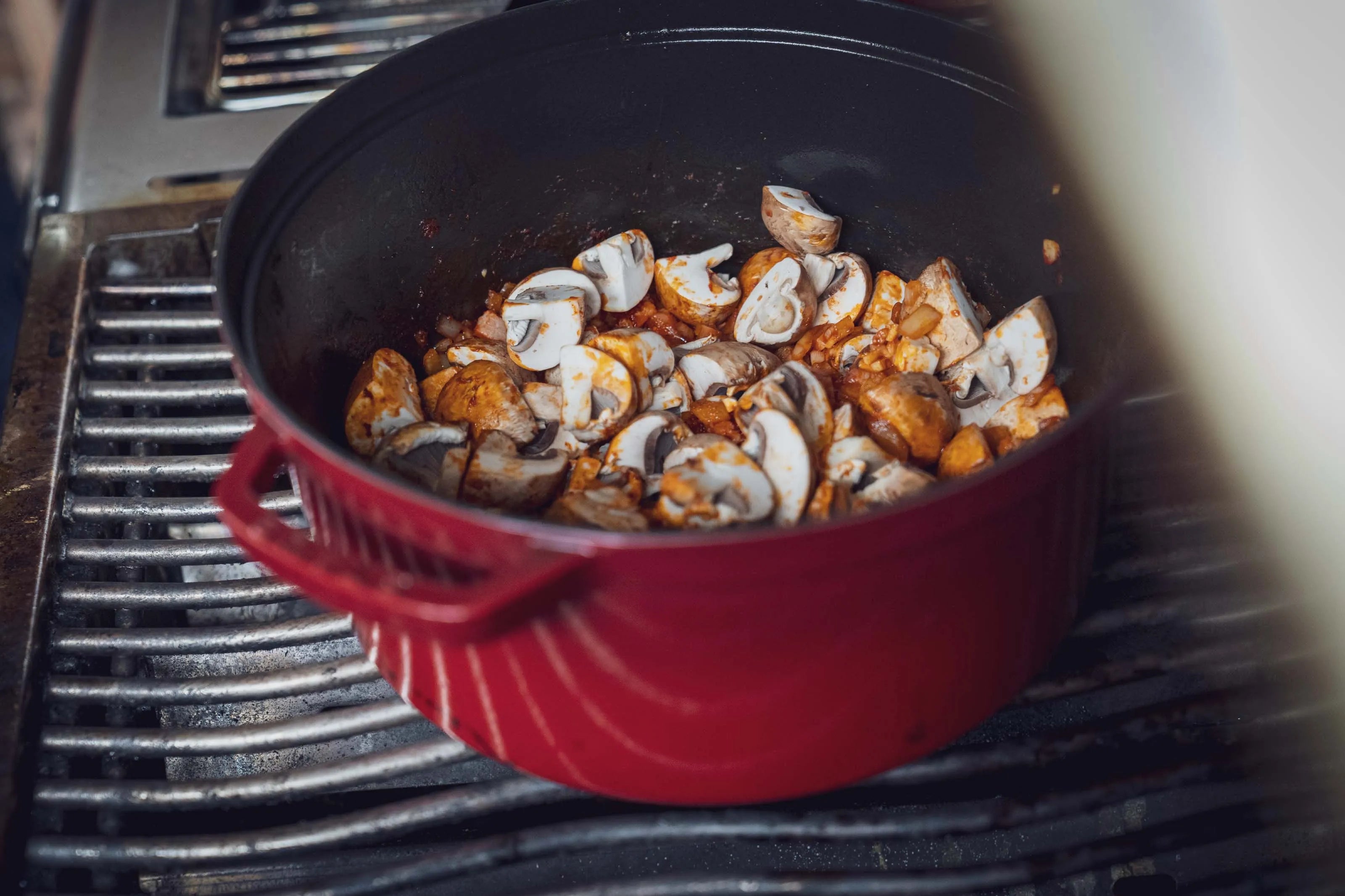Roter Topf auf Herd, gefüllt mit Pilzen und Zwiebeln.