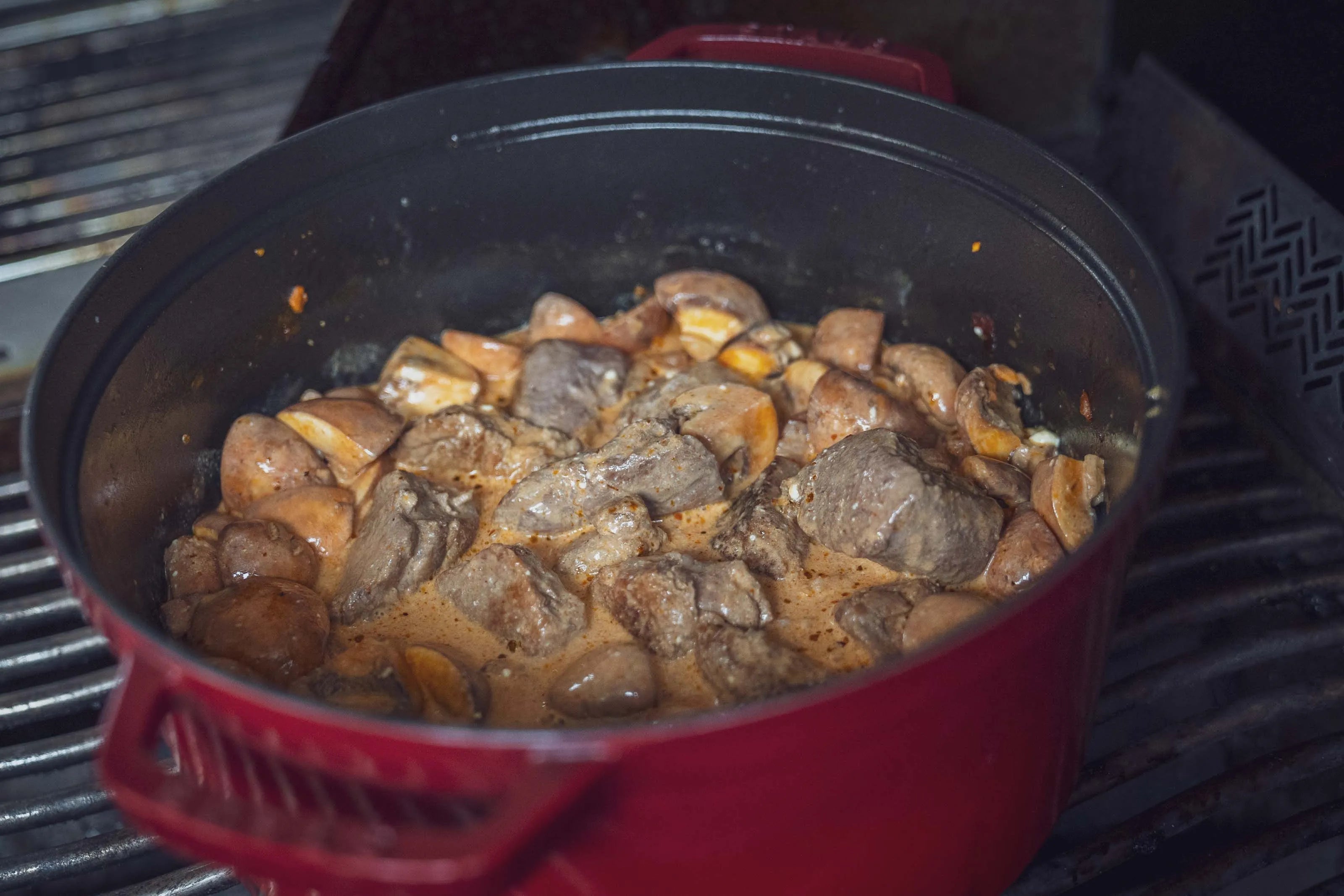 Eintopf mit Fleischstücken in rotem Topf auf Herd.