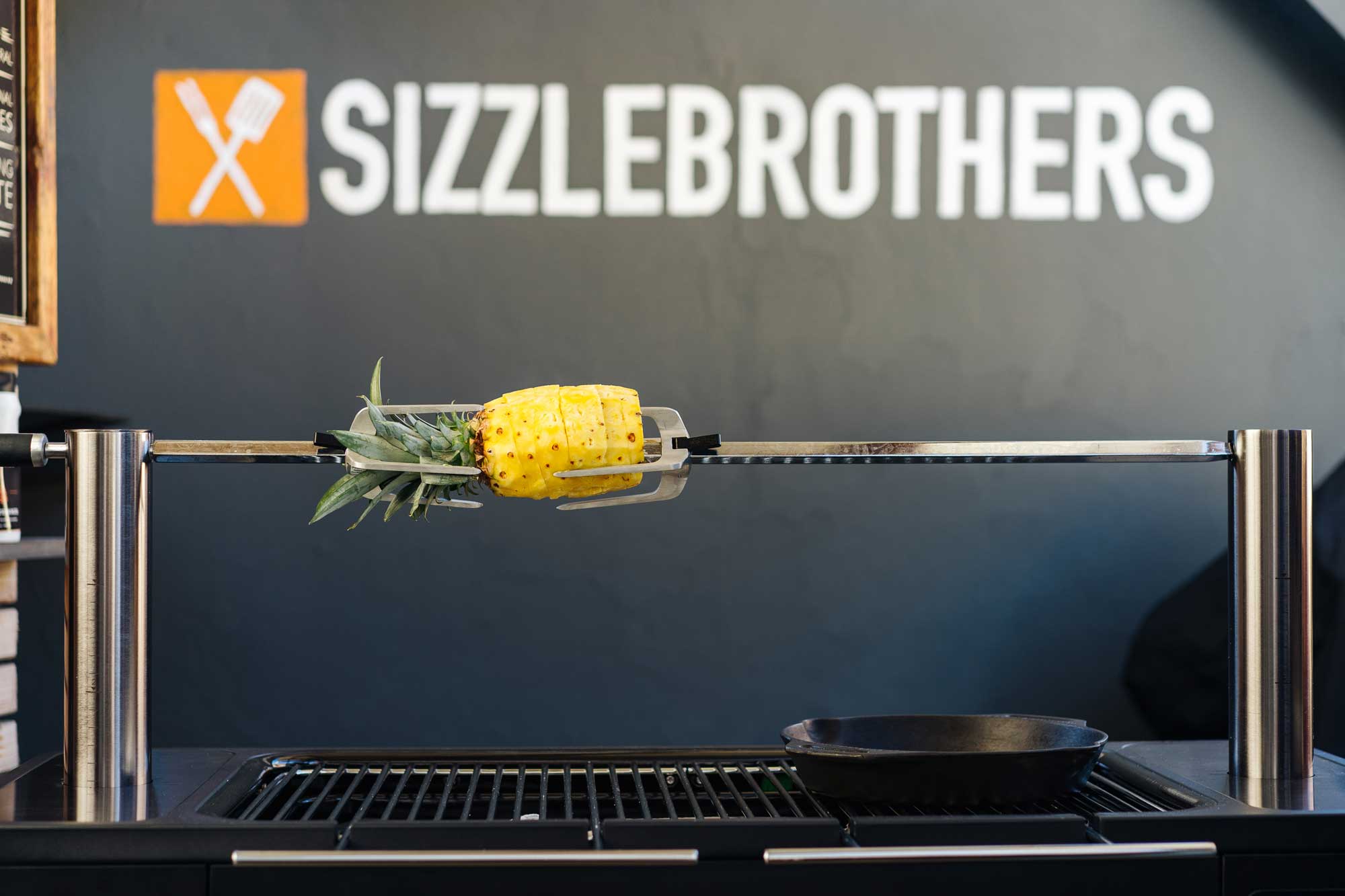 Eine ausgehöhlte Ananas steckt auf einem Drehspieß und dreht sich über der Glut