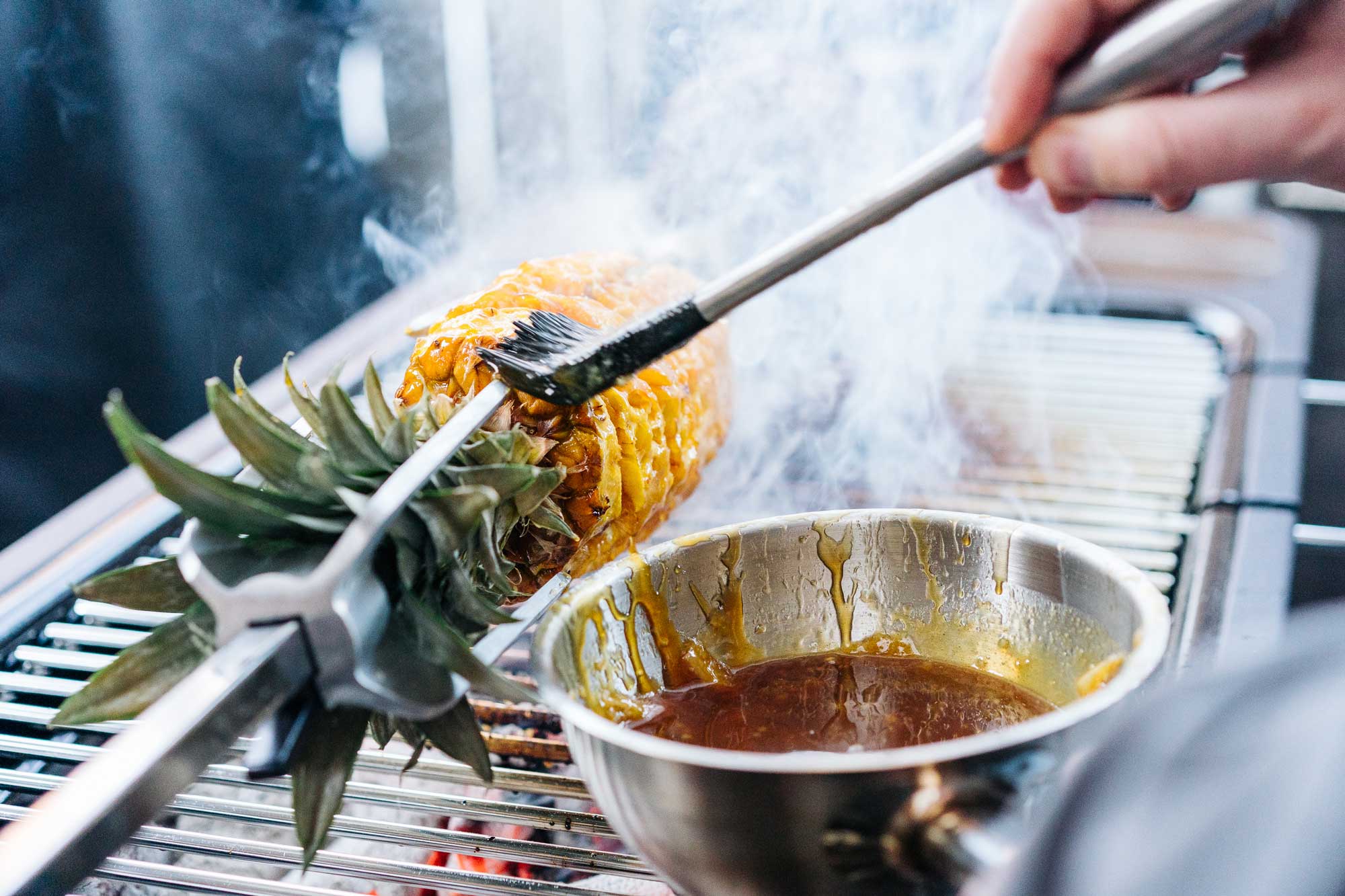 Die Ananas auf dem Drehspieß wird mit Karamell bestrichen