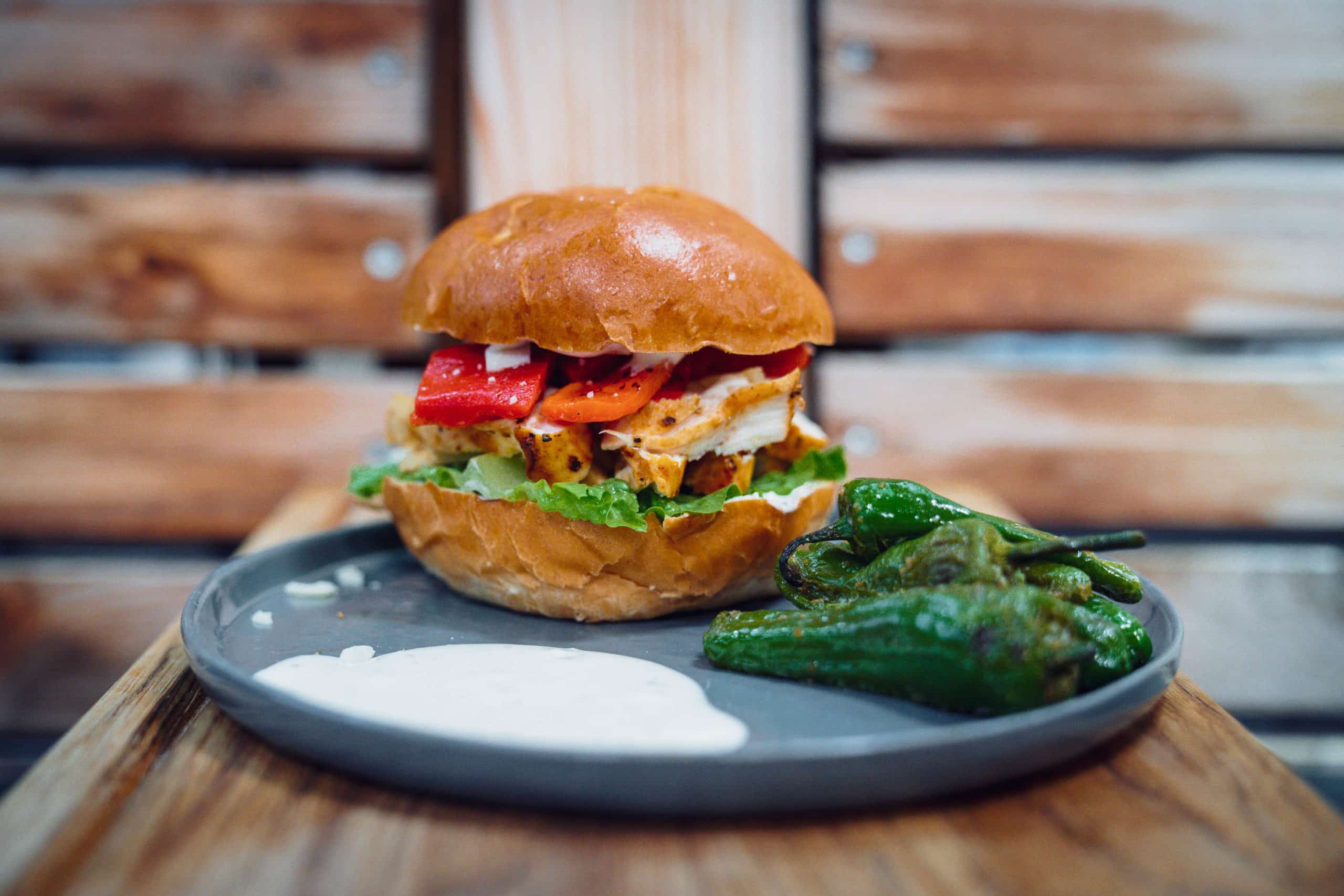 Burger mit Paprika und Salat auf Teller, daneben gebratene grüne Paprika und weiße Sauce.