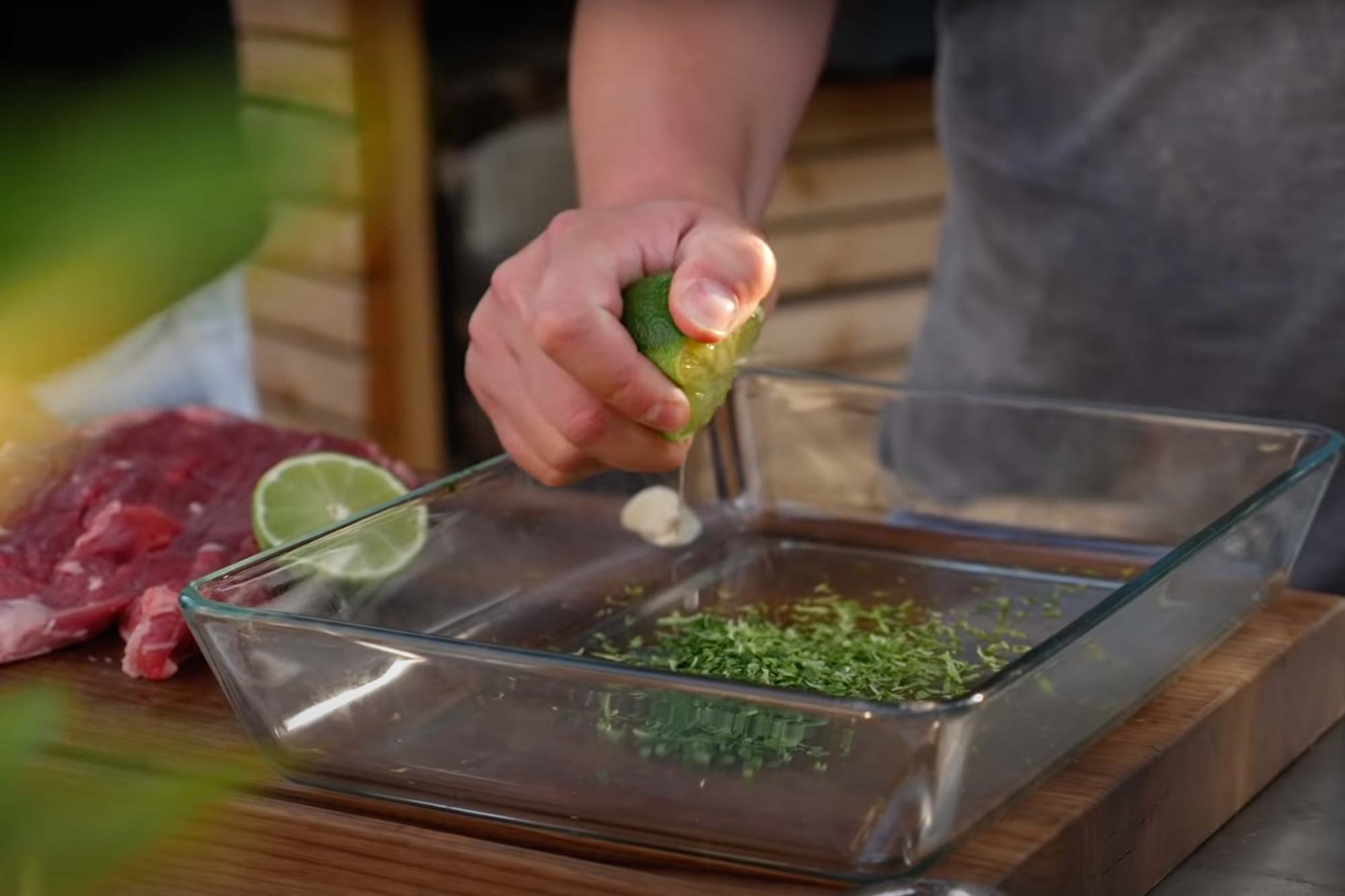 Person drückt Limettensaft in eine Glasschale mit gehackten Kräutern.