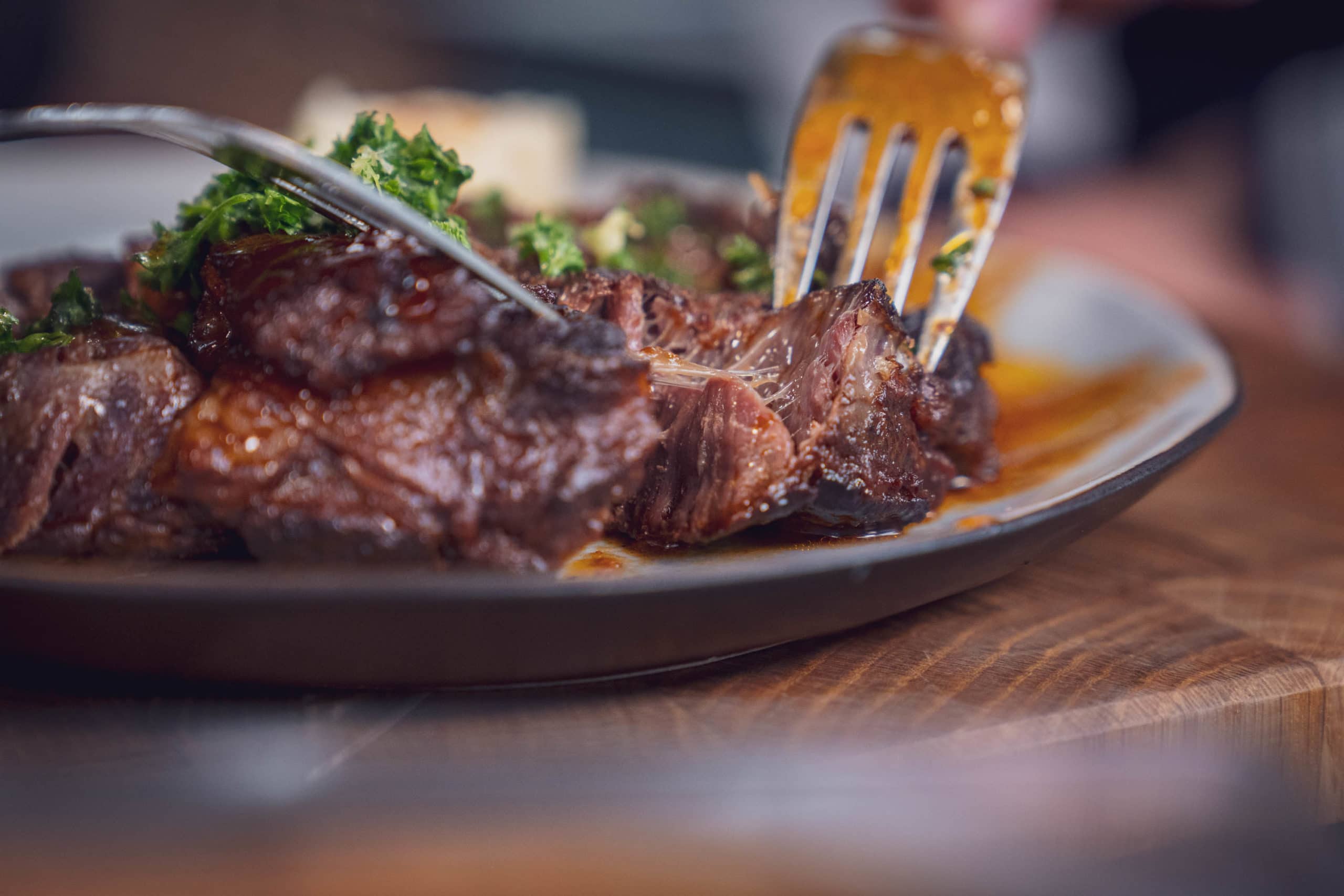 Nahaufnahme eines großen Fleischstücks mit Gabel und Messer auf einem Teller.