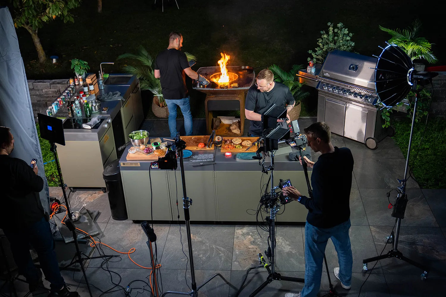 Nachtaufnahme einer Outdoor-Küche mit zwei Grillköchen und zwei Kameraleuten.