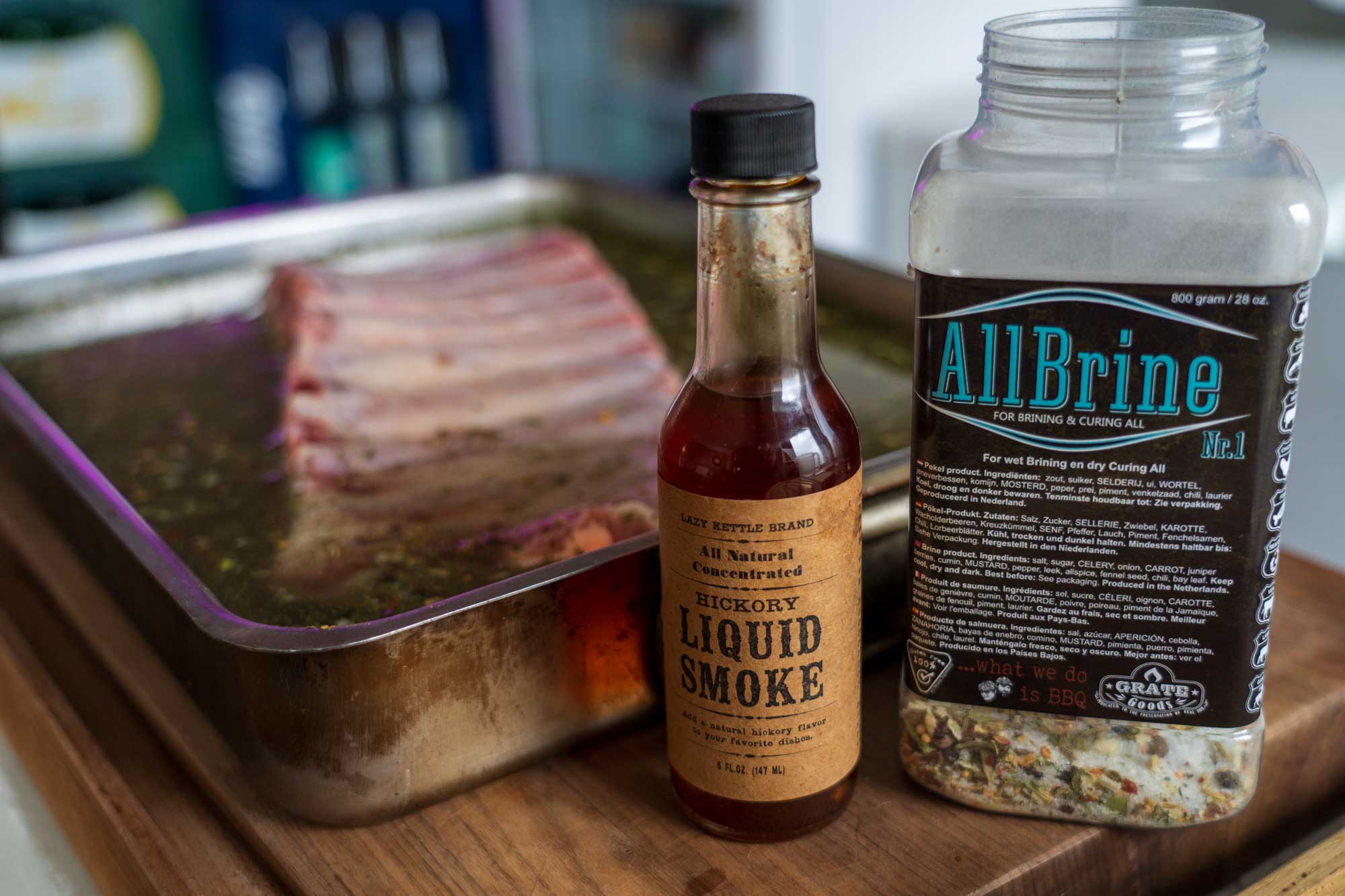 Flasche Liquid Smoke und Glas mit Brine neben geräucherten Rippchen.