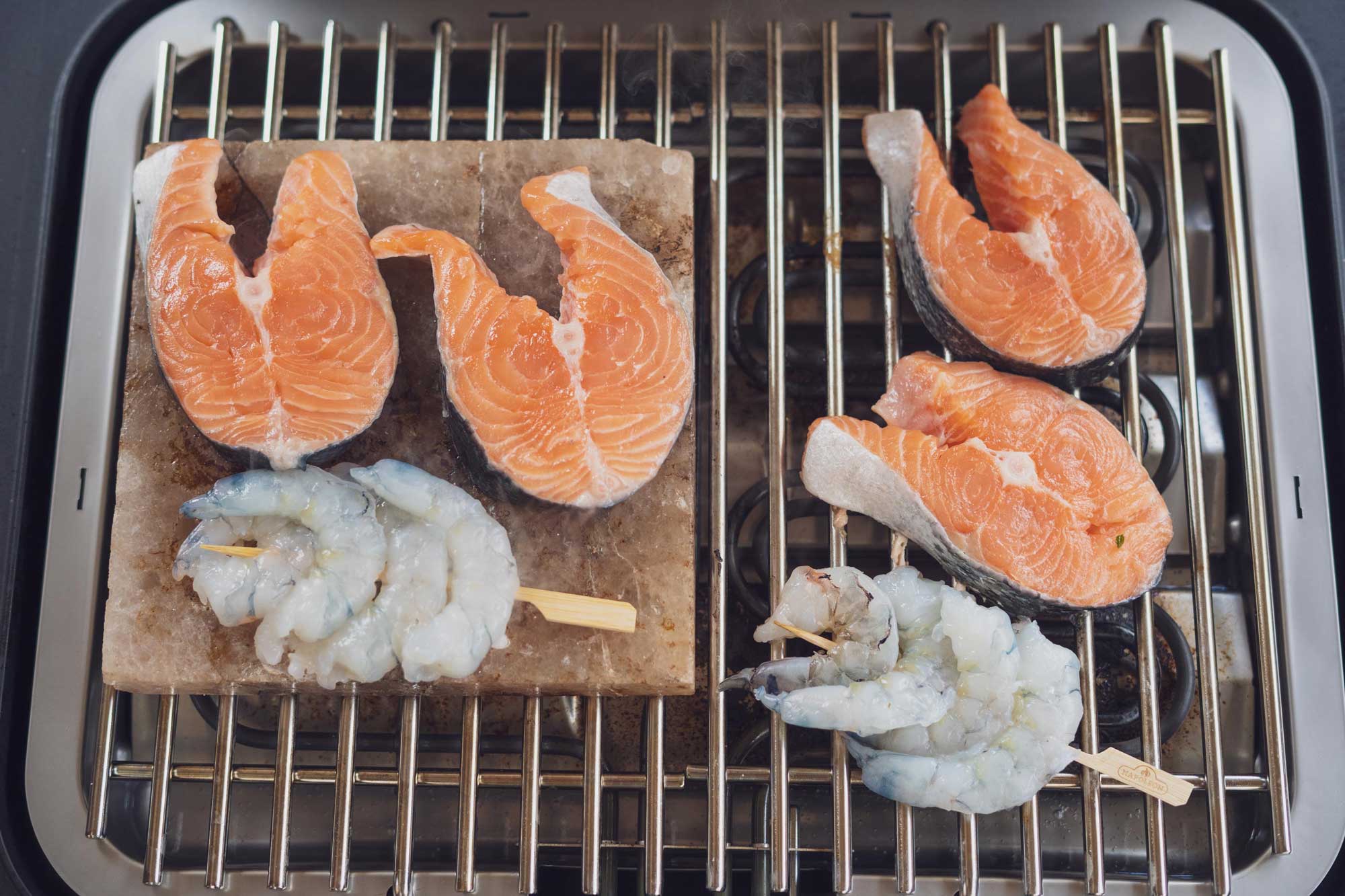 Lachs und Garnelen liegen auf dem Grill bzw. den Salzstein