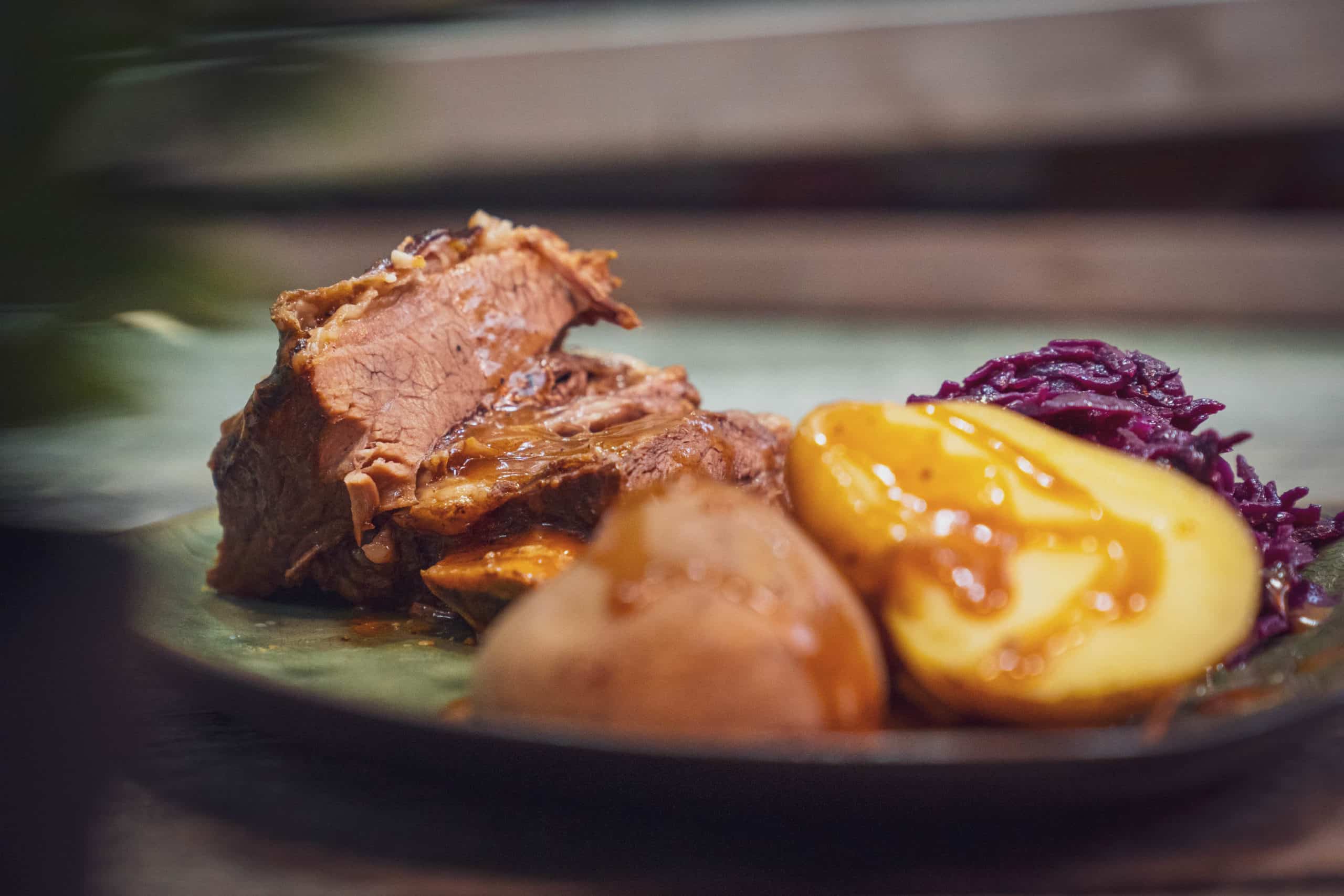 Kochfleisch, Kartoffelhälfte und Rotkraut auf einem Teller.
