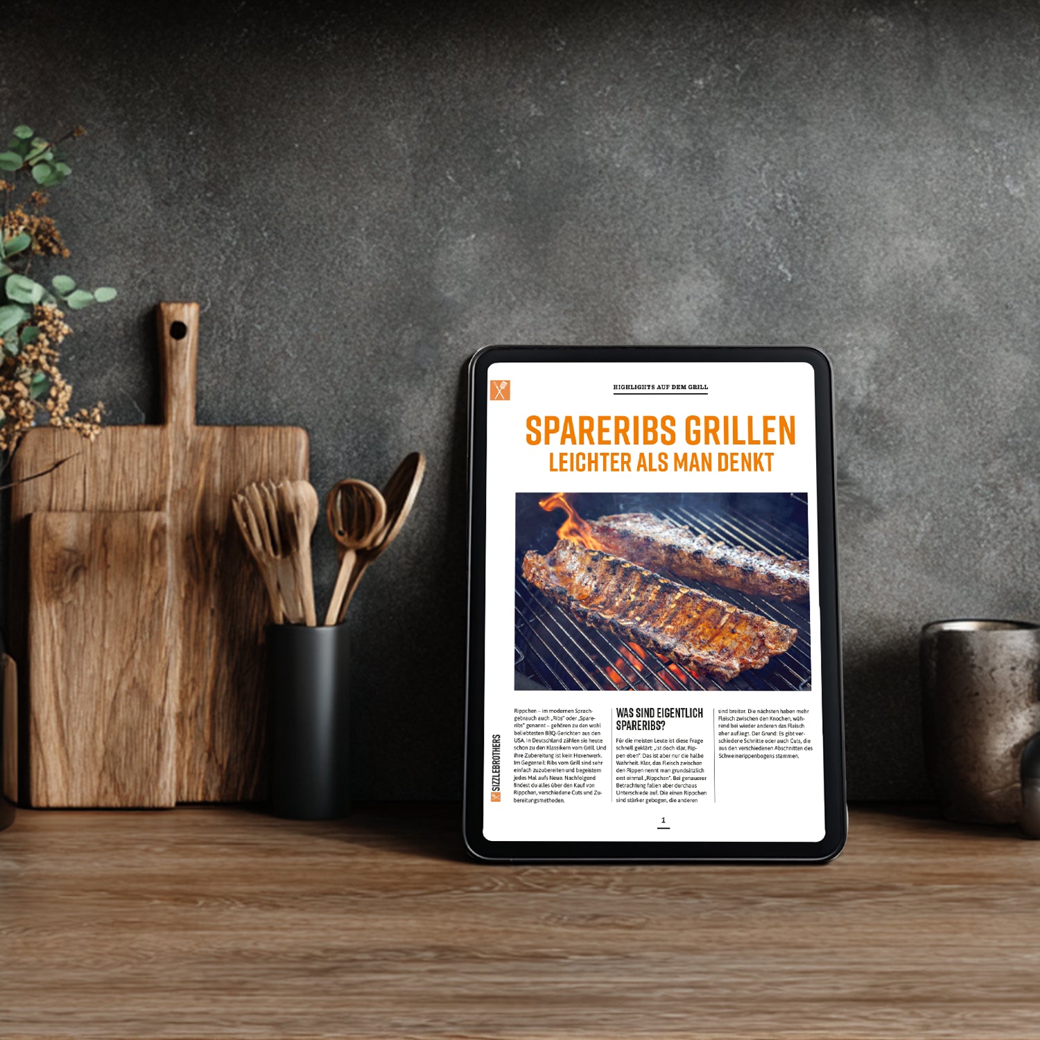 Tablet auf Holzarbeitsfläche zeigt Spareribs-Rezept, daneben Kochutensilien und Pflanzen.