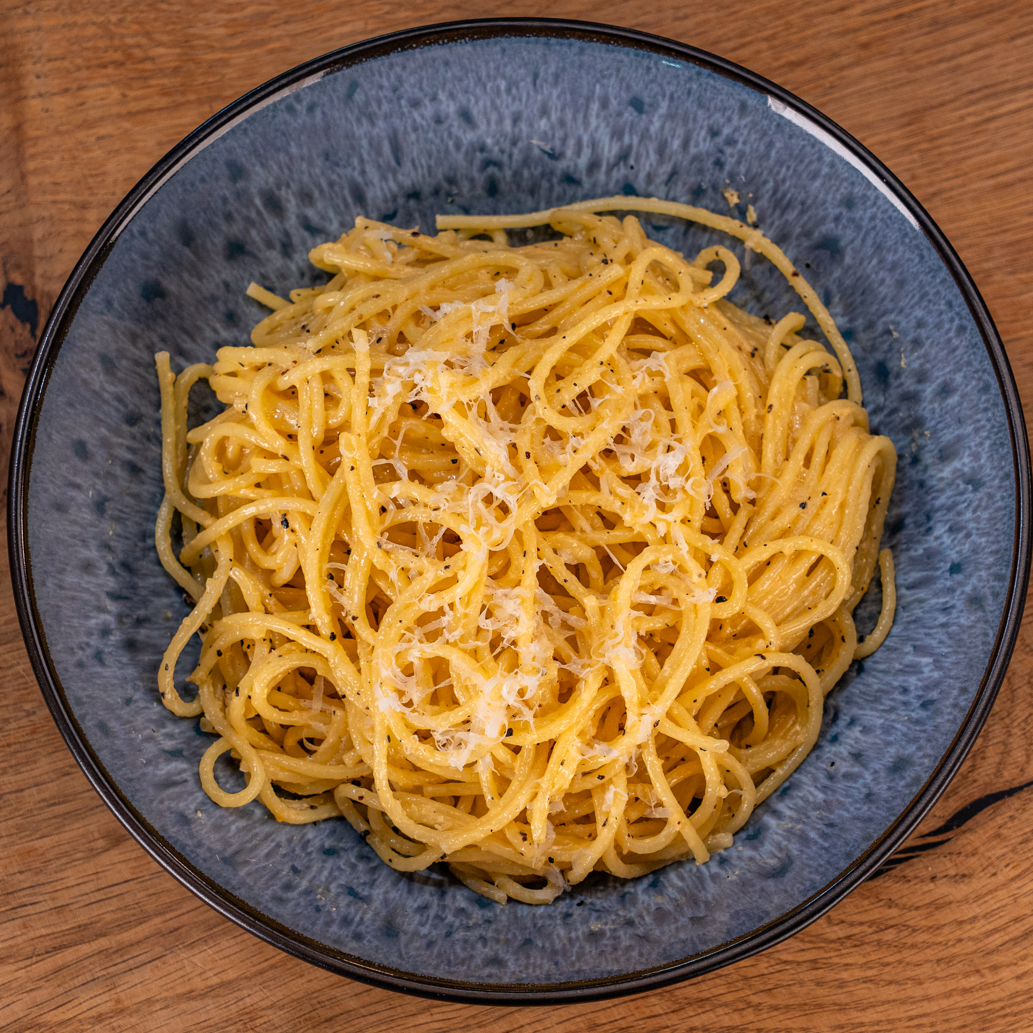 Spaghetti mit geriebenem Käse auf einem blauen Teller auf Holztisch.