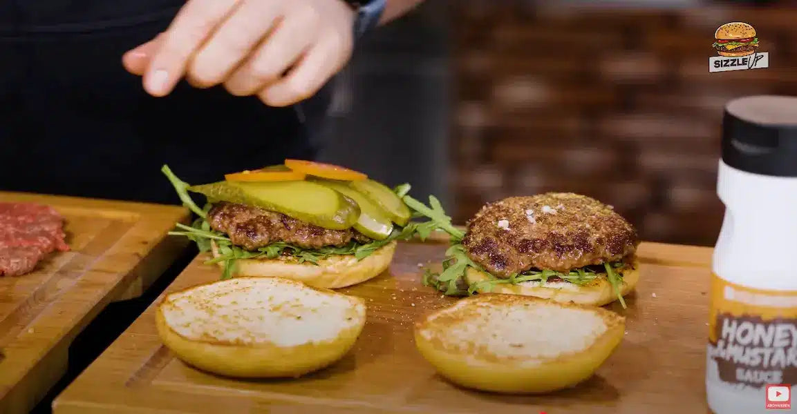 Burgerbrötchen für Ziegenkäse Burger mit BBQ-Sauce, Rucola Rindfleisch-Pattie und Gewürzgurke belegen