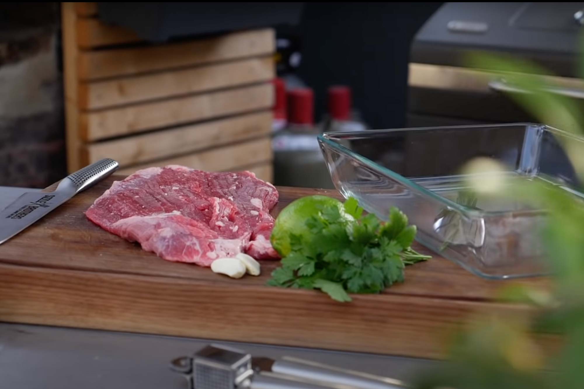 Rohes Steak, Limette, Koriander und Knoblauch auf einem Holzbrett mit Glasform daneben.