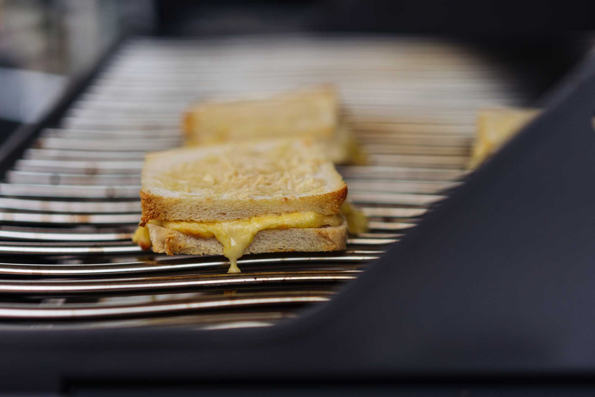 Auf einem Grill werden Sandwichscheiben angeröstet und Käse dazwischen geschmolzen