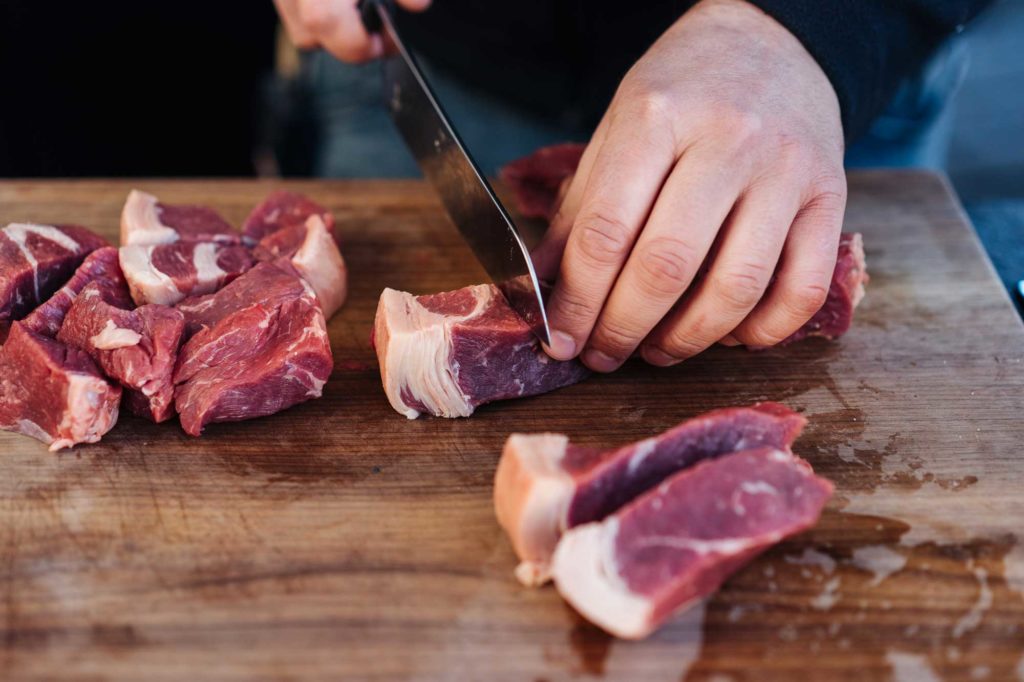Fleisch wird auf einem Brett in 2 x 2 cm groÃŸe StÃ¼cke geschnitten