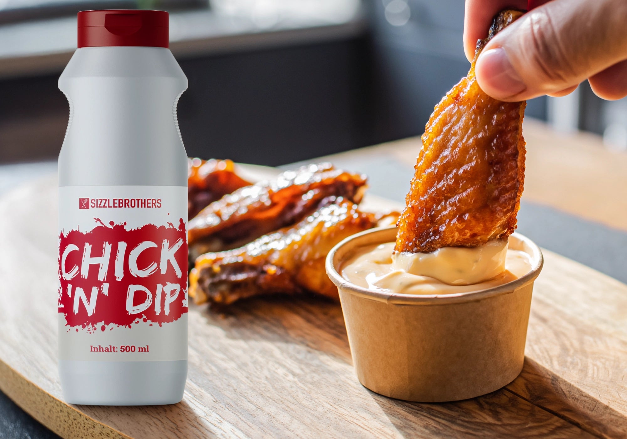 Flasche Chick 'N' Dip neben Hühnerflügel, die in orangene Soße getunkt werden.