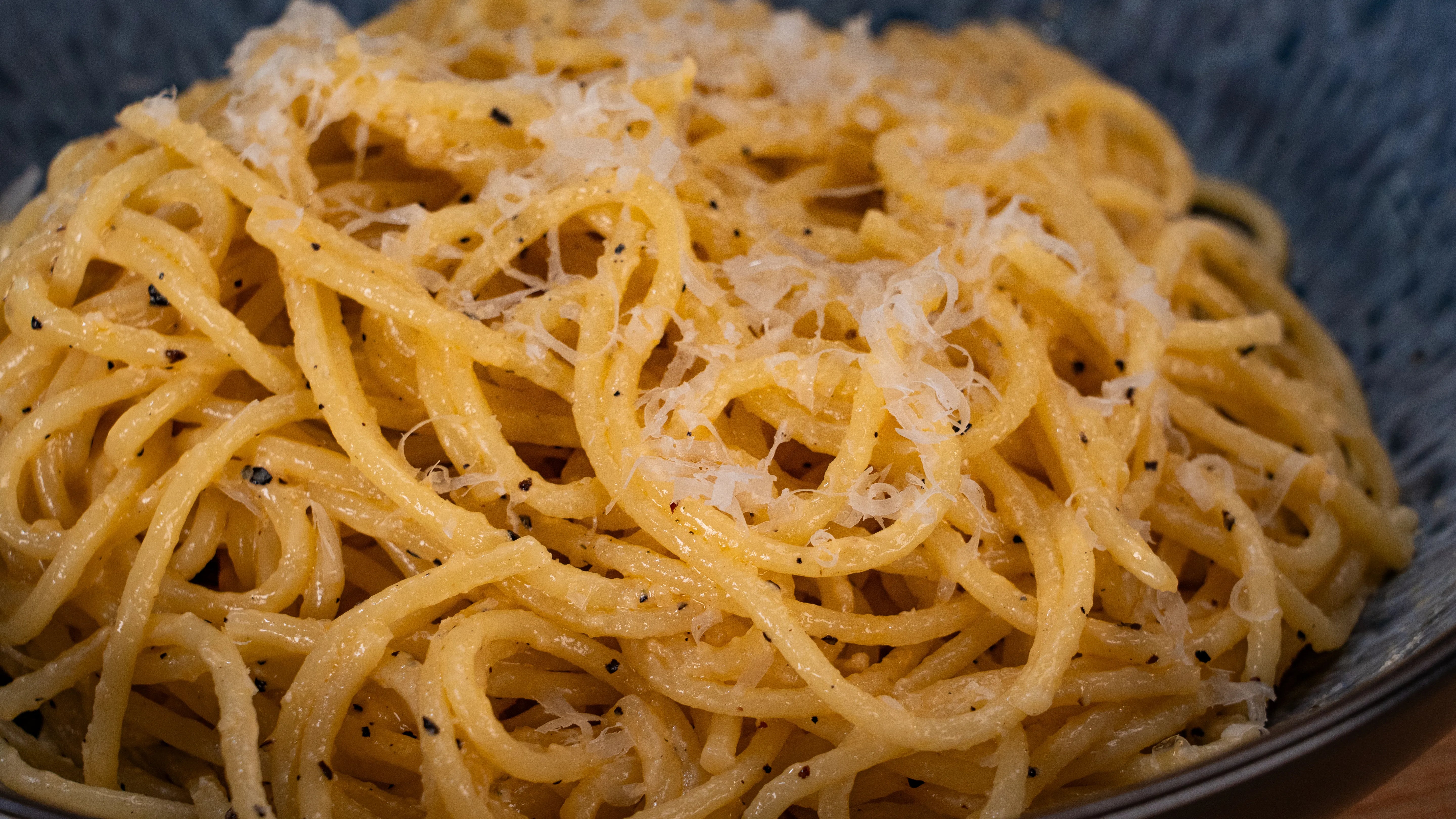 Spaghetti mit Pfeffer und geriebenem Käse in einer blauen Schüssel.