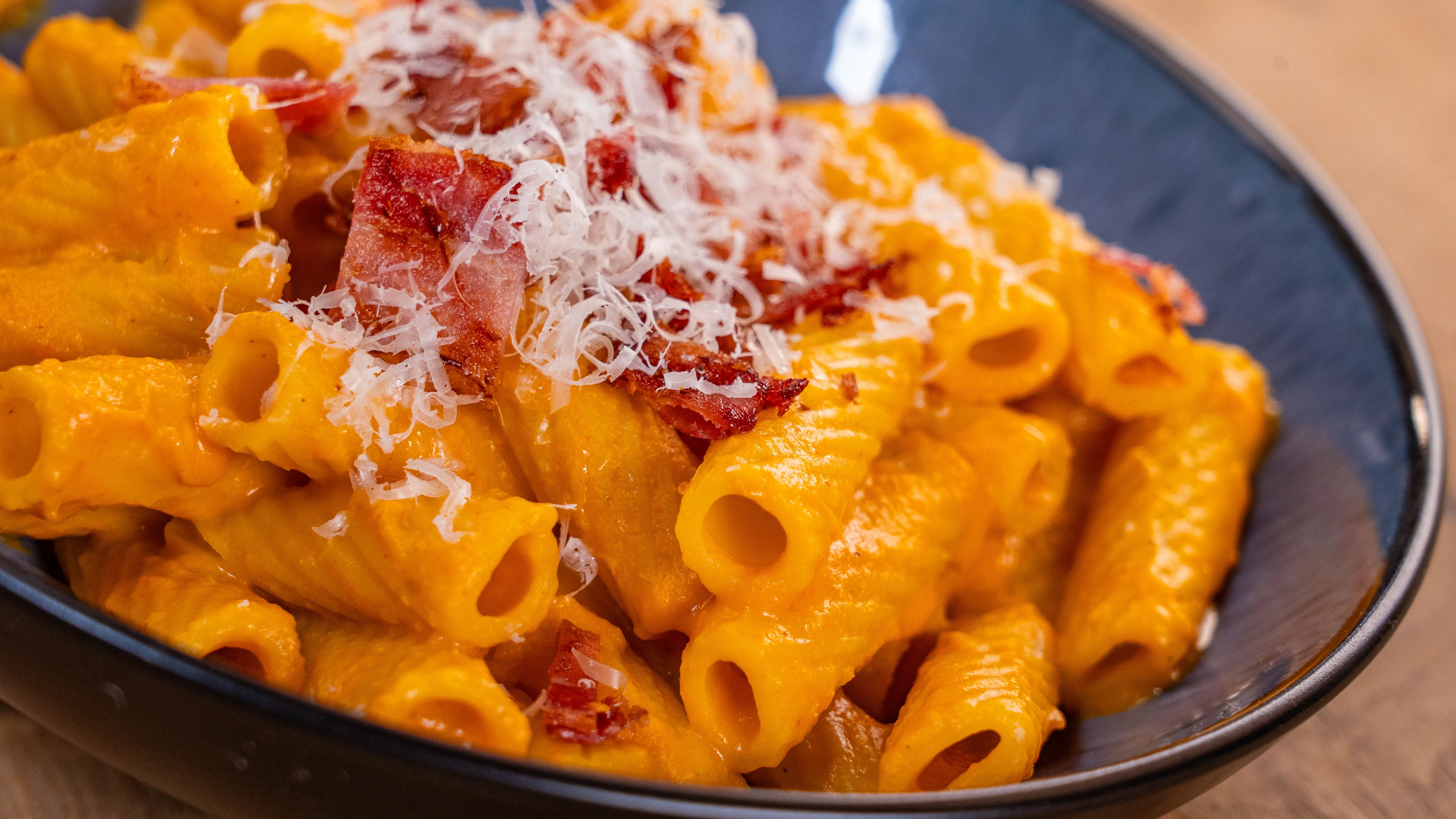 Nudeln mit Speckstückchen und geriebenem Käse in Schüssel serviert.