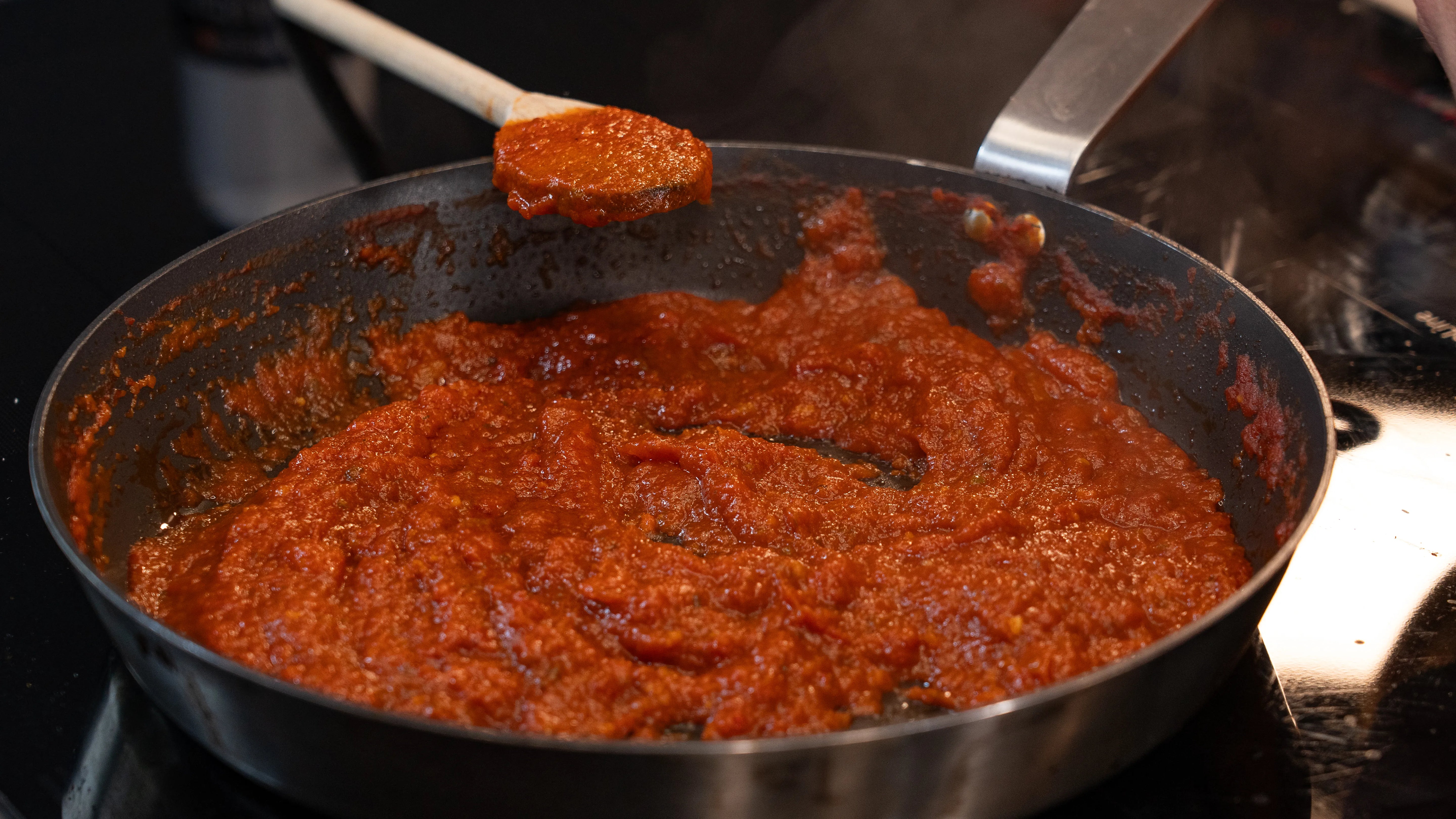 Dampfende Tomatensauce in einer Pfanne mit einem Holzlöffel.