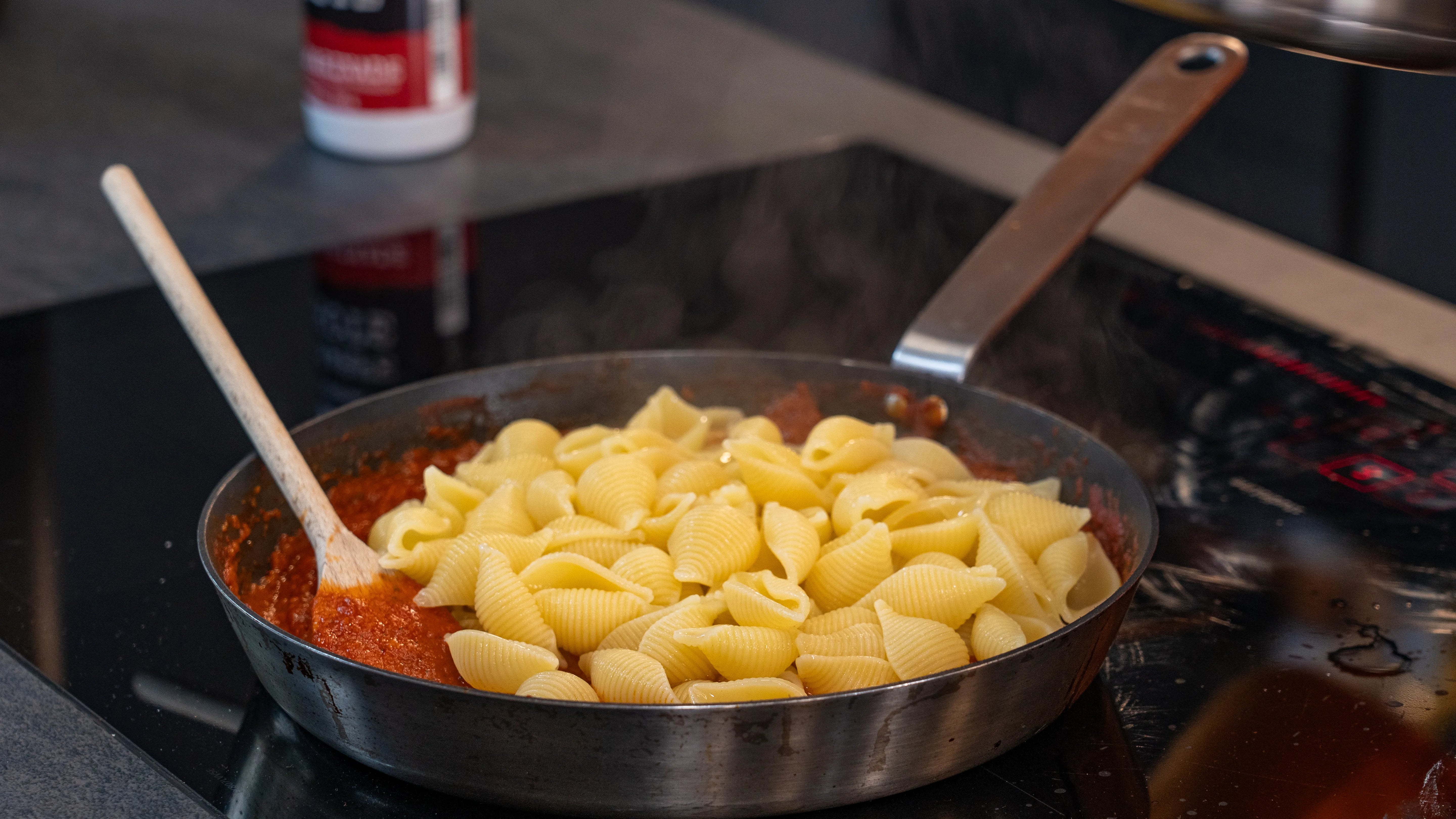 Muschelnudeln in roter Sauce in einer Pfanne mit Holzlöffel.