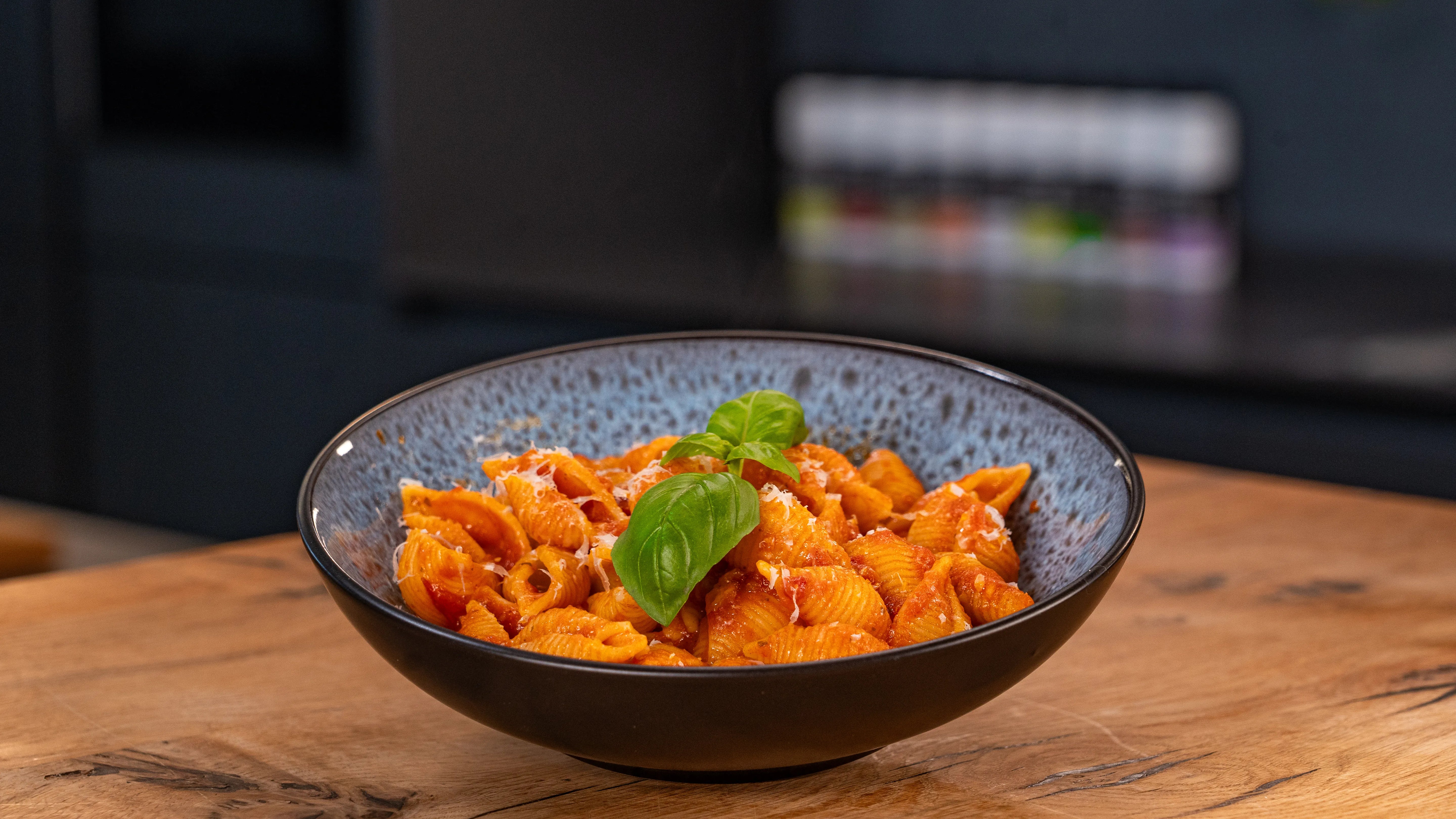 Schüssel mit roter Nudelsauce, garniert mit frischem Basilikum, auf einem Tisch.