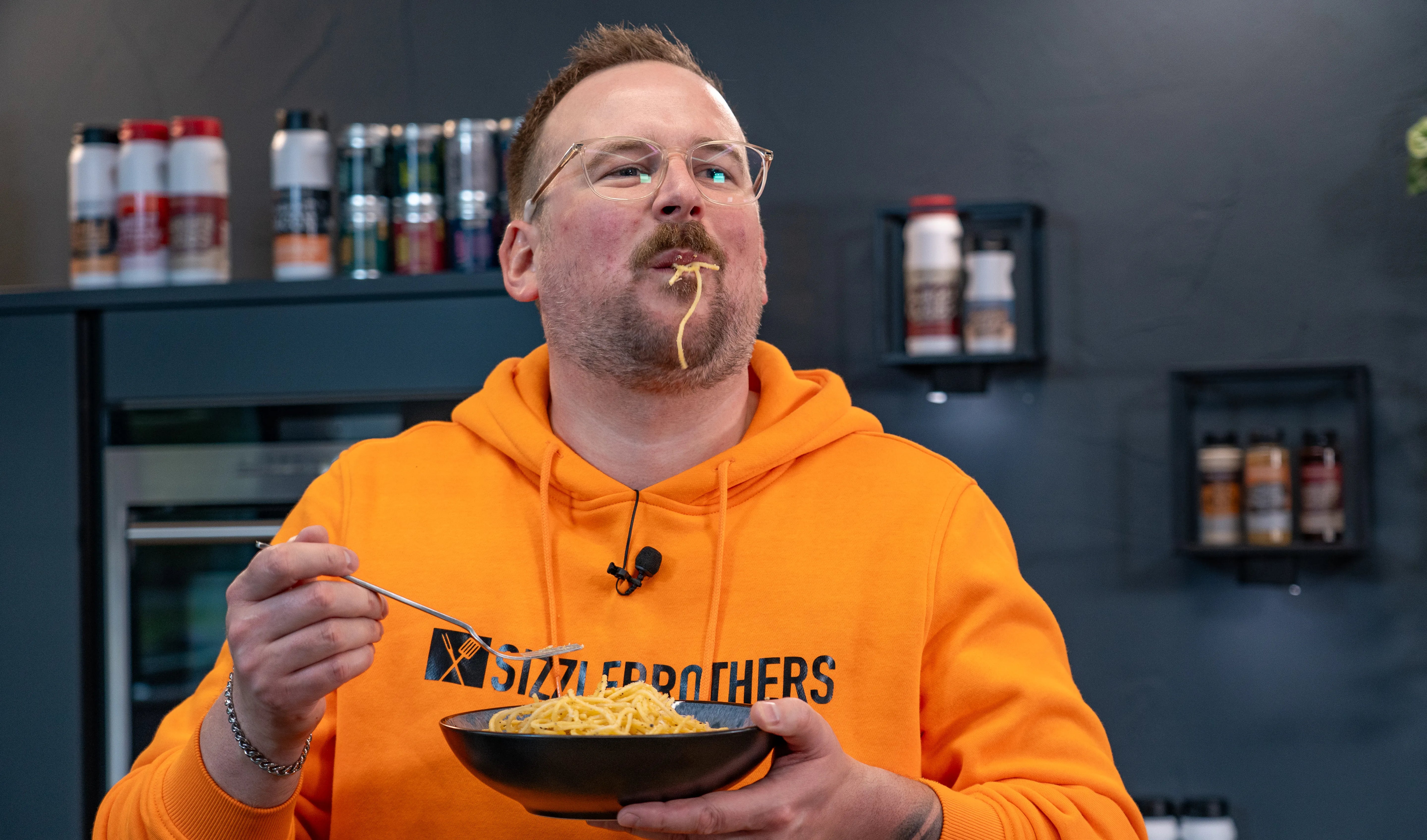 Person in orangefarbenem Hoodie isst Spaghetti mit einer Gabel.