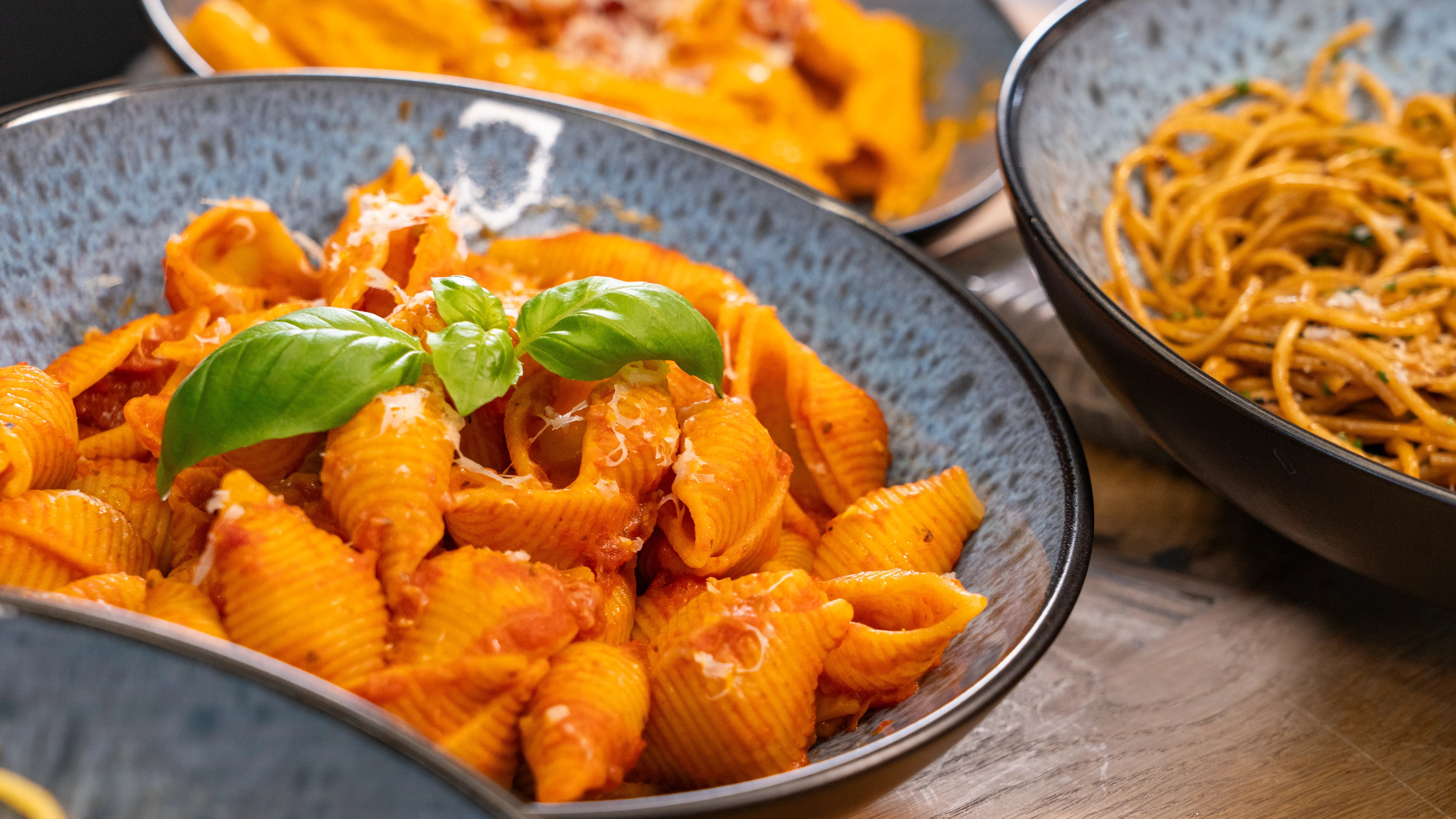 Nudelgericht mit Tomatensoße und Basilikum in einer blauen Schüssel.