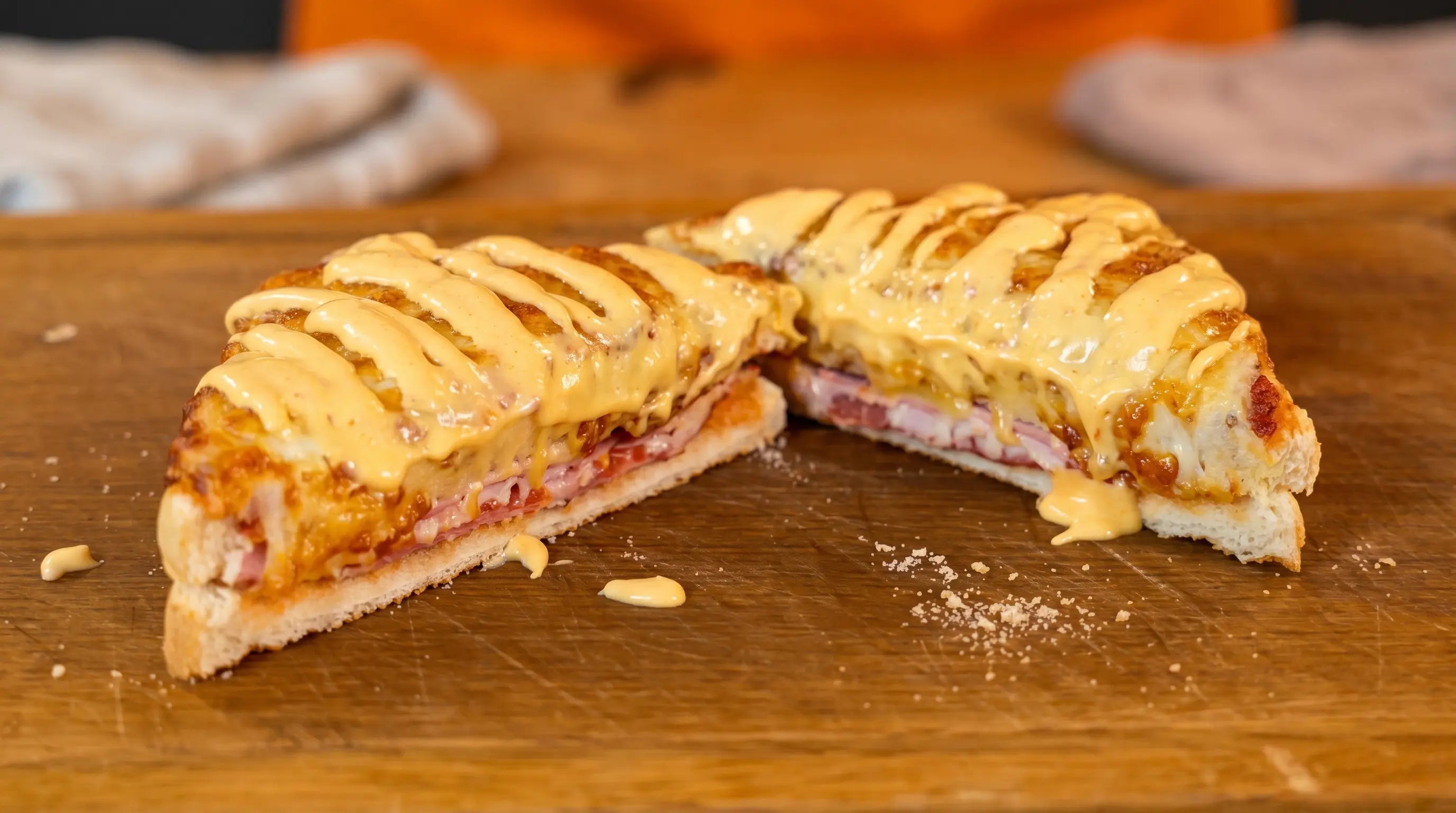 Ein halbiertes Sandwich mit Schinken, Käse und Sauce auf einem Holzbrett.