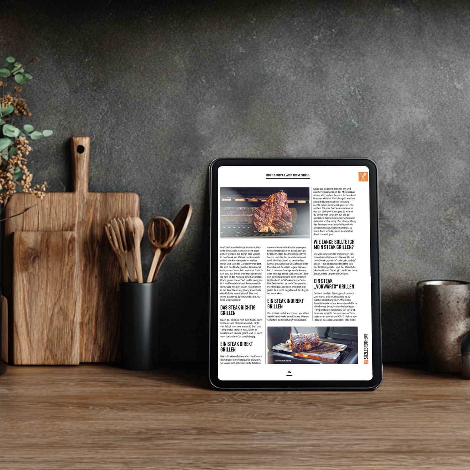 Tablet in Küche zeigt Grillbilder und Text über Grillmethoden neben Utensilien.