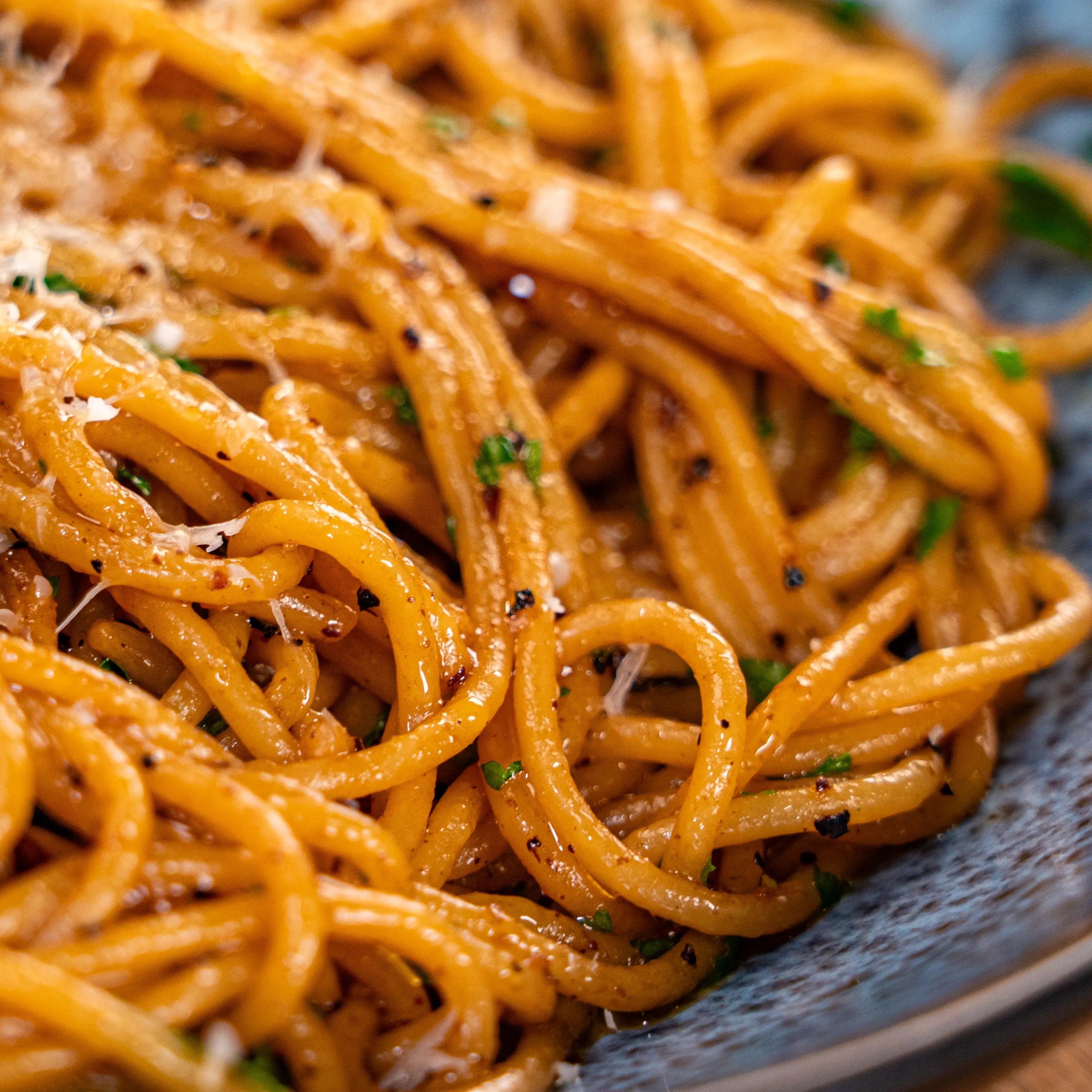 Nahaufnahme von Spaghetti mit Kräutern und Parmesan auf grauem Teller.