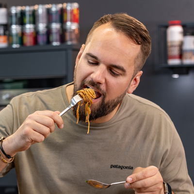 Person isst Spaghetti mit einer Gabel in der Küche.