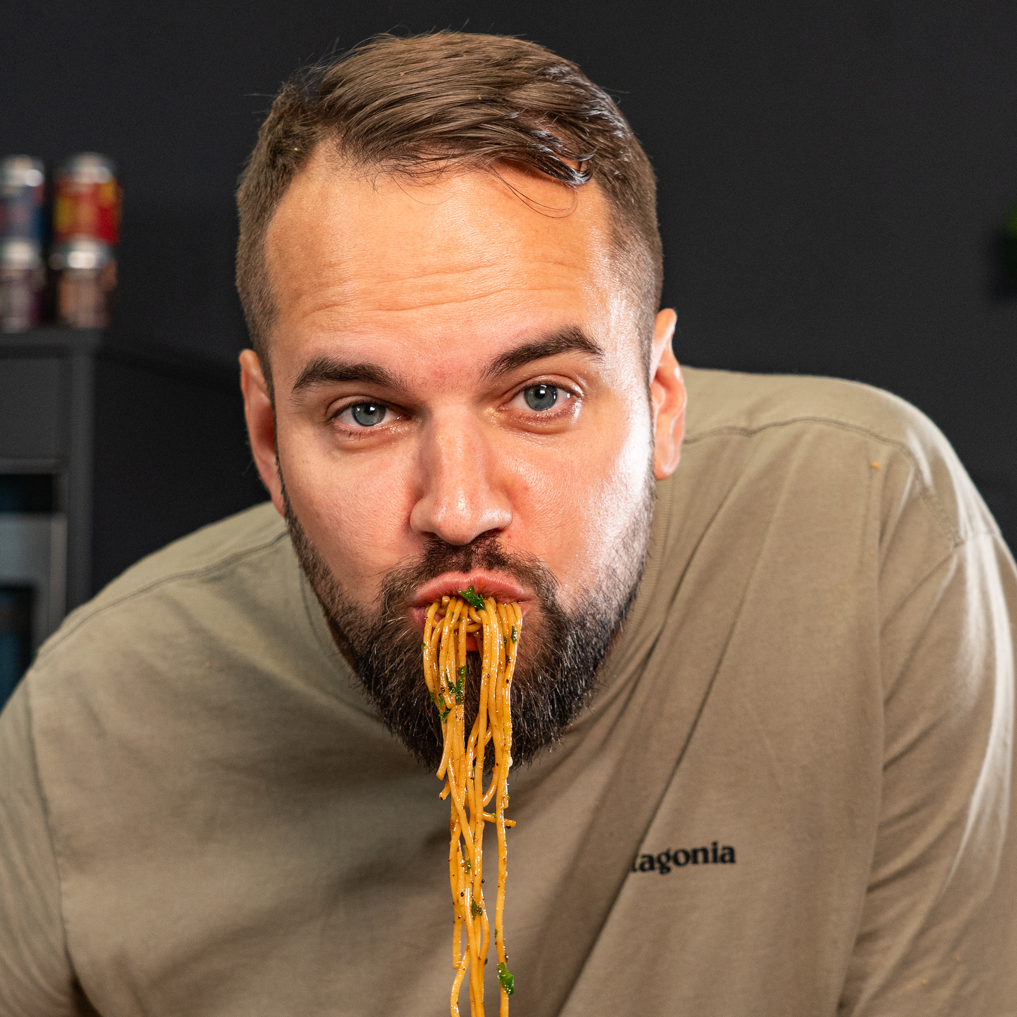 Person mit Spaghetti im Mund, stellt sich vor dunklem Hintergrund vor.