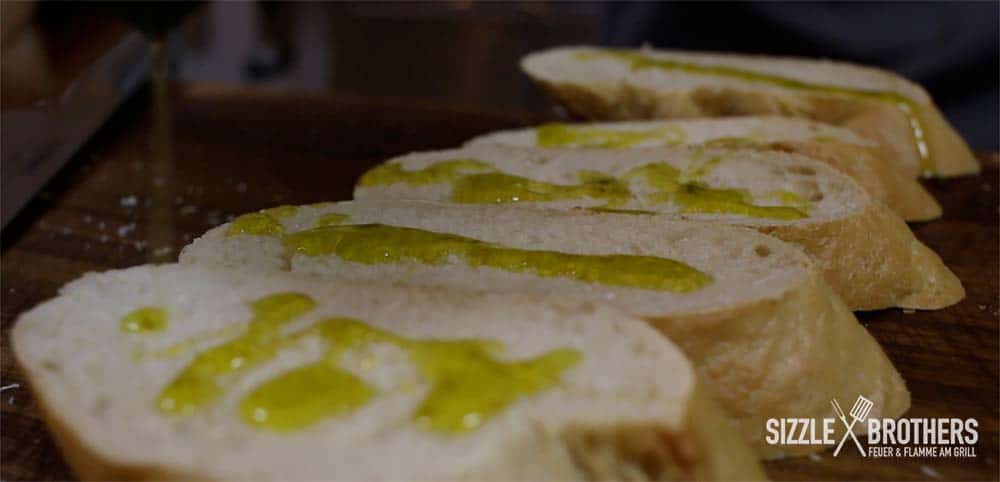 Das aufgeschnittene Baguette wird mit Olivenöl eingestrichen