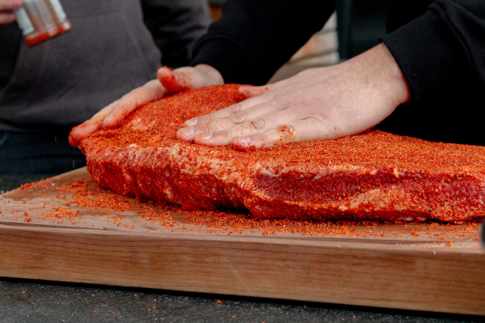 Das Beef Brisket Texas Style wird auf einem Holzbrett mit Gewürz eingerieben