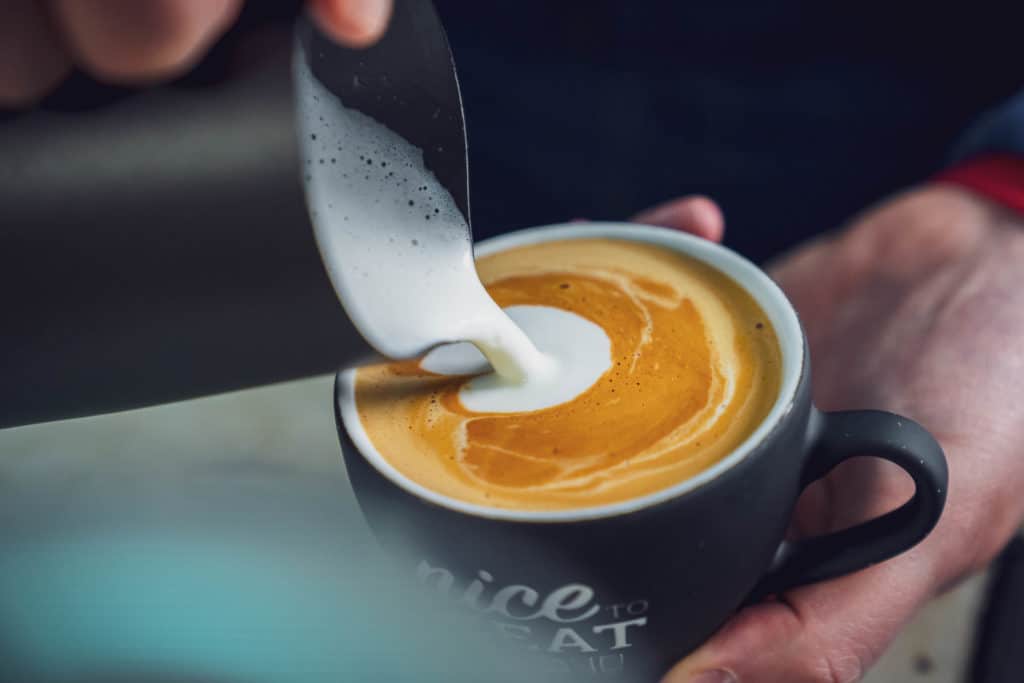 Milch wird für den Cappuccino in die Tasse gegeben